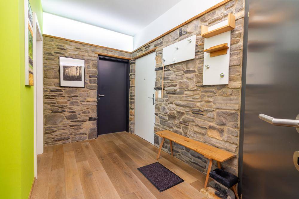 Eingangsbereich mit Steinwandverkleidung, Holzboden und Garderobe.