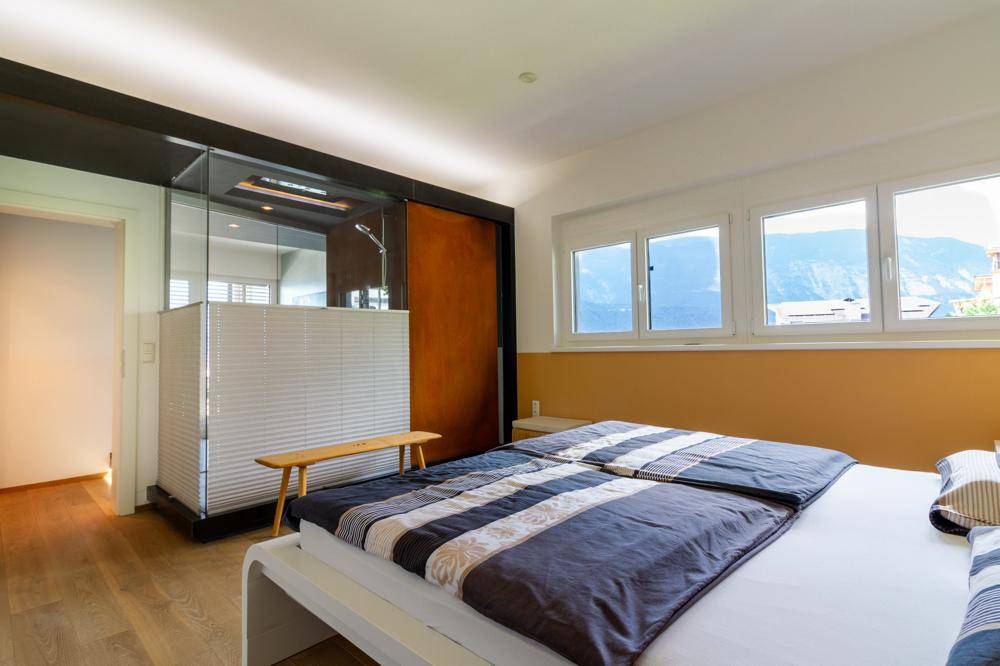 Schlafzimmer mit Holzboden, modernem Bett und integriertem Duschbereich.