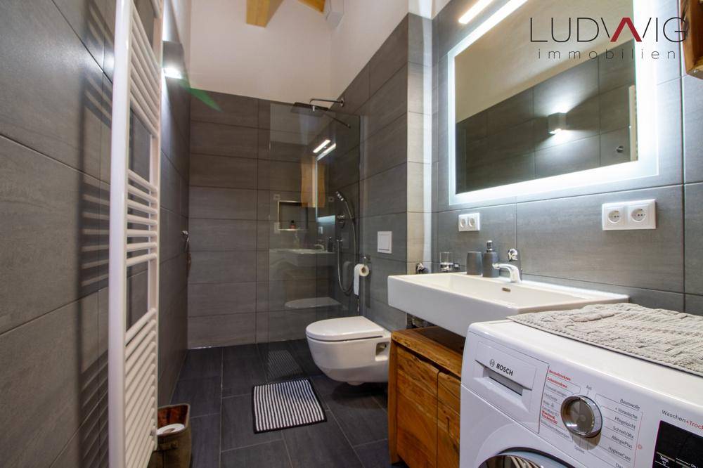 Modernes Badezimmer mit großer begehbarer Dusche, beheiztem Handtuchhalter und Waschmaschine.