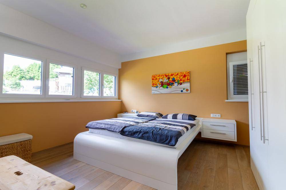 Helles Schlafzimmer mit modernem Bett, Holzboden und gelber Akzentwand.