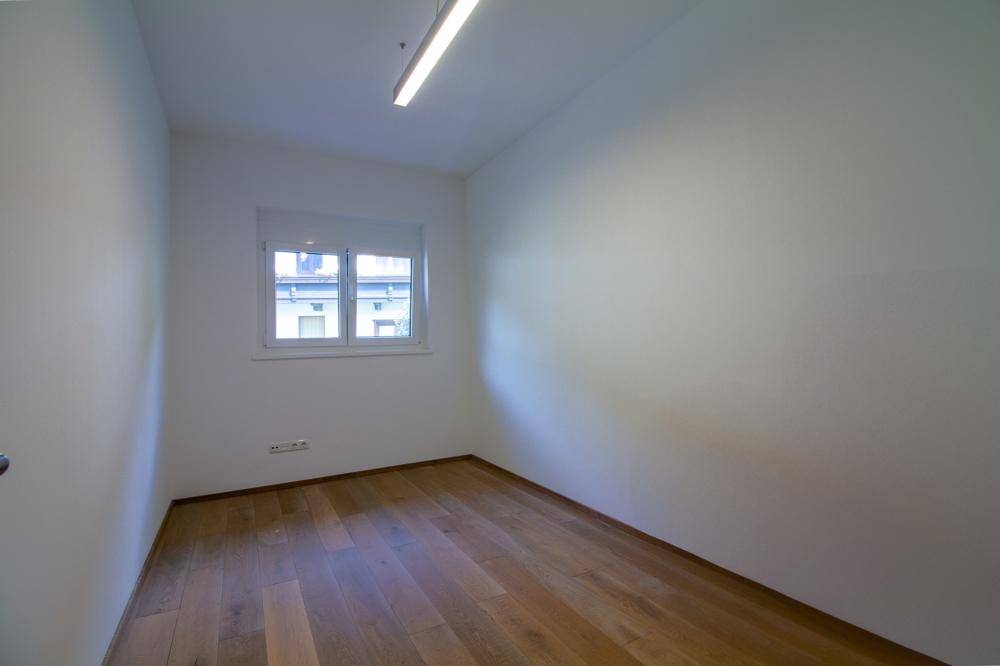 Leeres Zimmer mit Holzboden, weißen Wänden und einem Fenster.