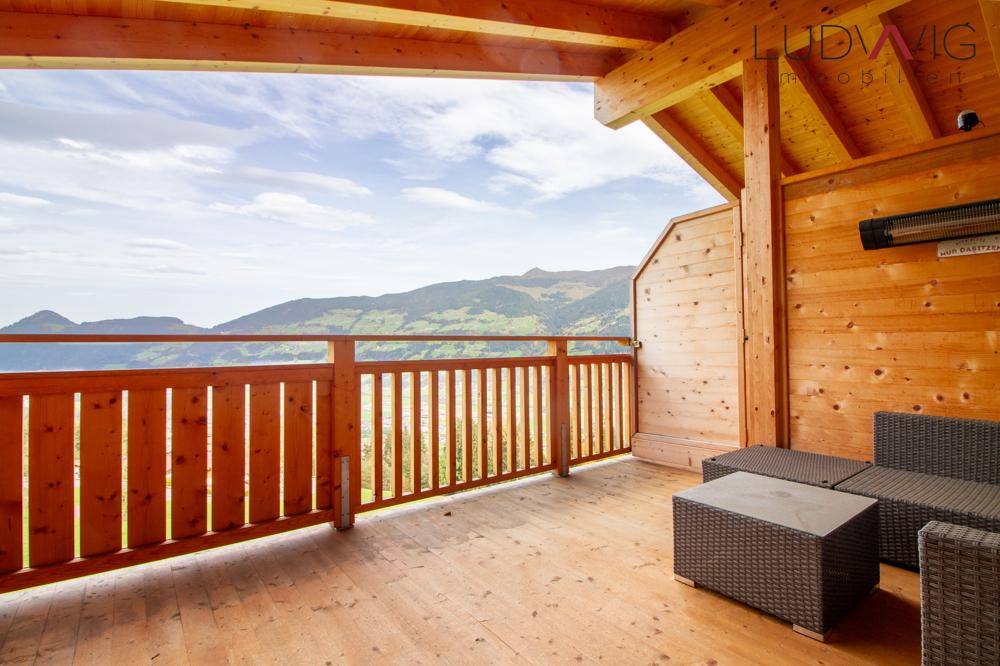 Geräumiger Holzbalkon mit Sitzgelegenheiten und weitem Blick auf die Berglandschaft.