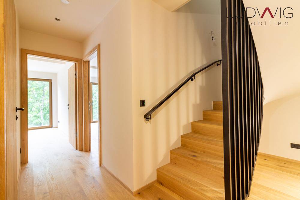 Heller Flur mit Holztreppe und modernem Geländer, der zu weiteren Zimmern führt.
