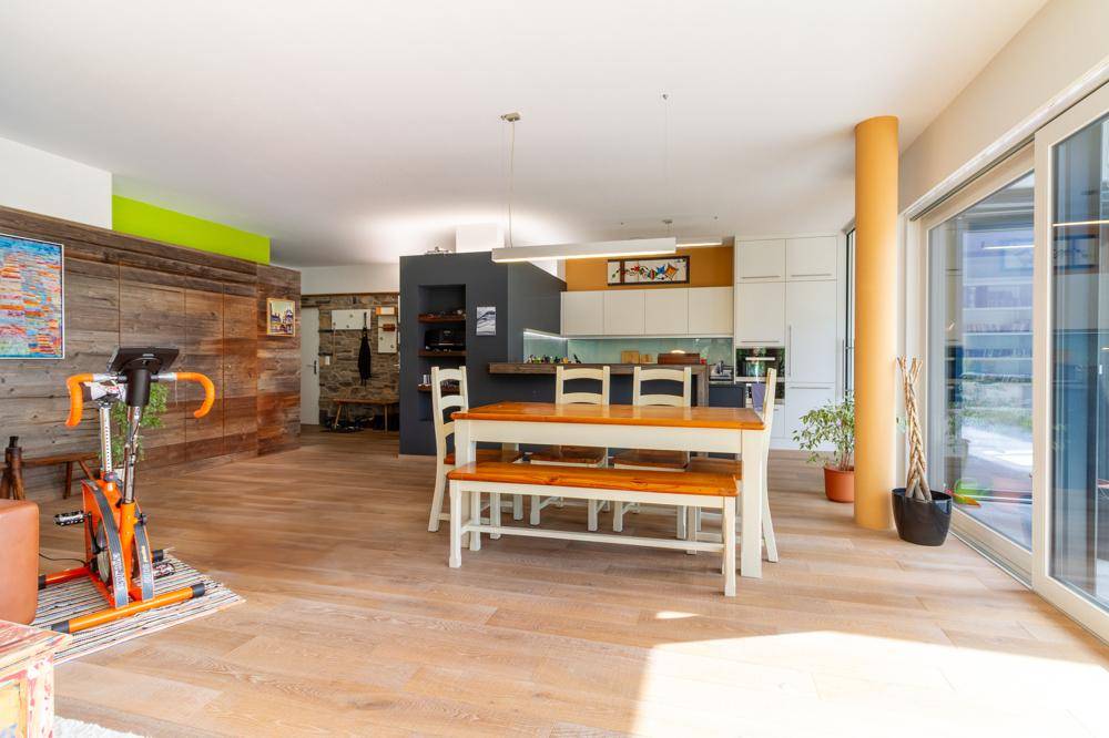 Offener Wohnbereich mit Holzboden, Essbereich und moderner Küche im Hintergrund.