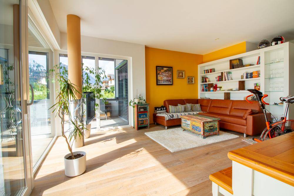 Gemütliches Wohnzimmer mit Ledersofa, gelber Akzentwand und Terrassenzugang.