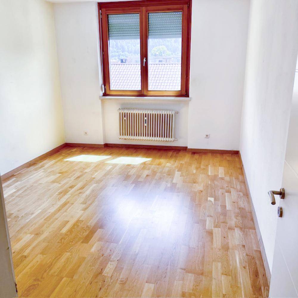 Leerer Raum mit Holzboden, großem Fenster und Heizkörper.