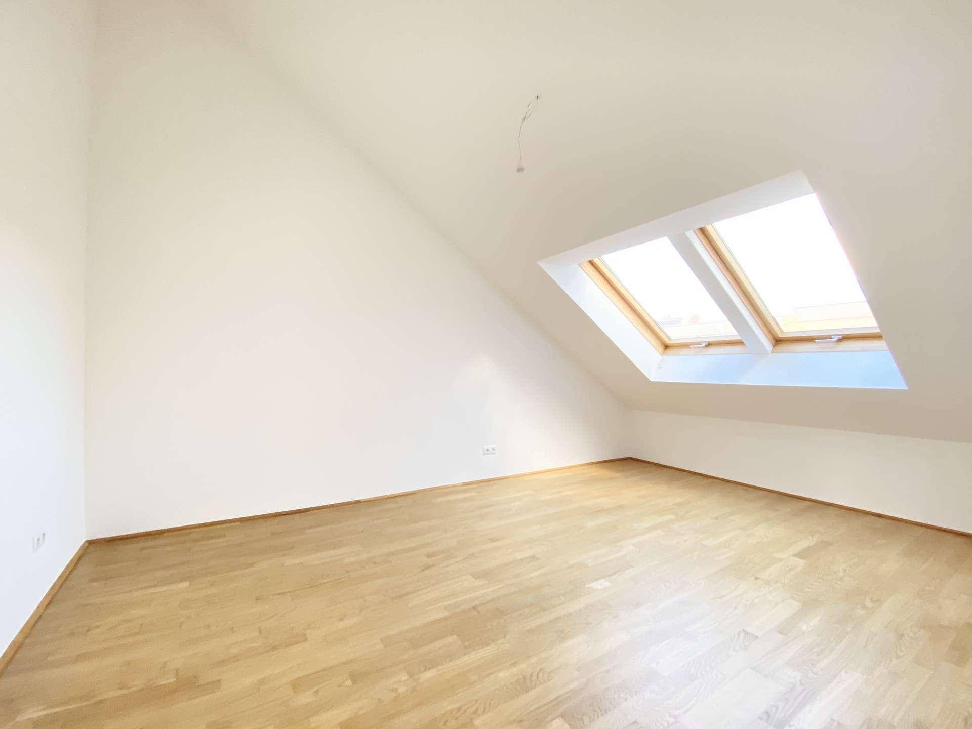 Geräumiges Zimmer mit Holzfußboden, weißen Wänden und zwei Dachfenstern, die den Raum erhellen.