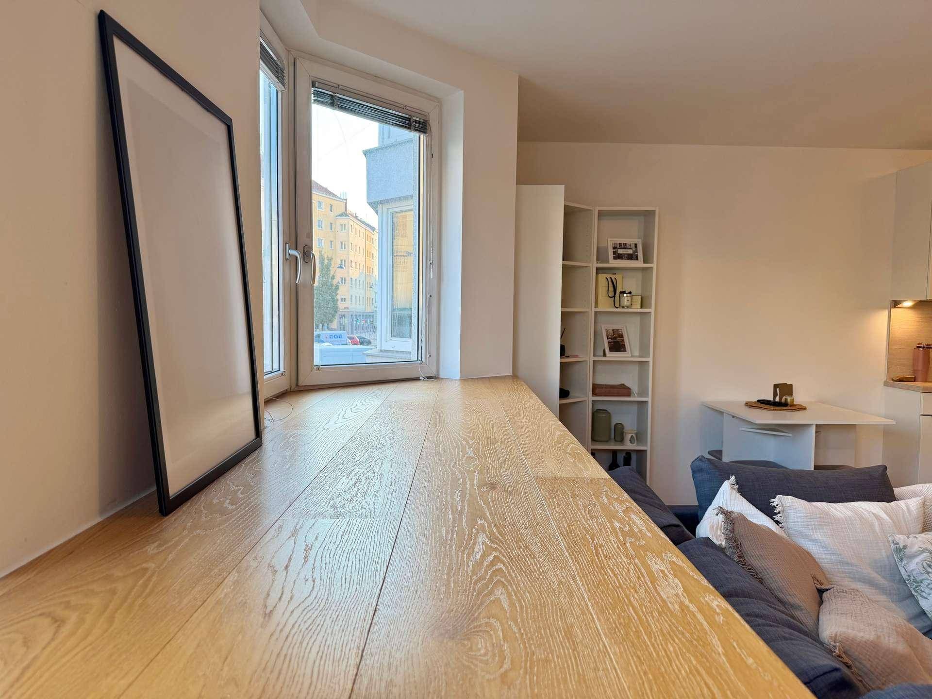 Heller Wohnbereich mit breiter Holzfensterbank und Blick auf die Stadt, ergänzt durch ein Sofa.