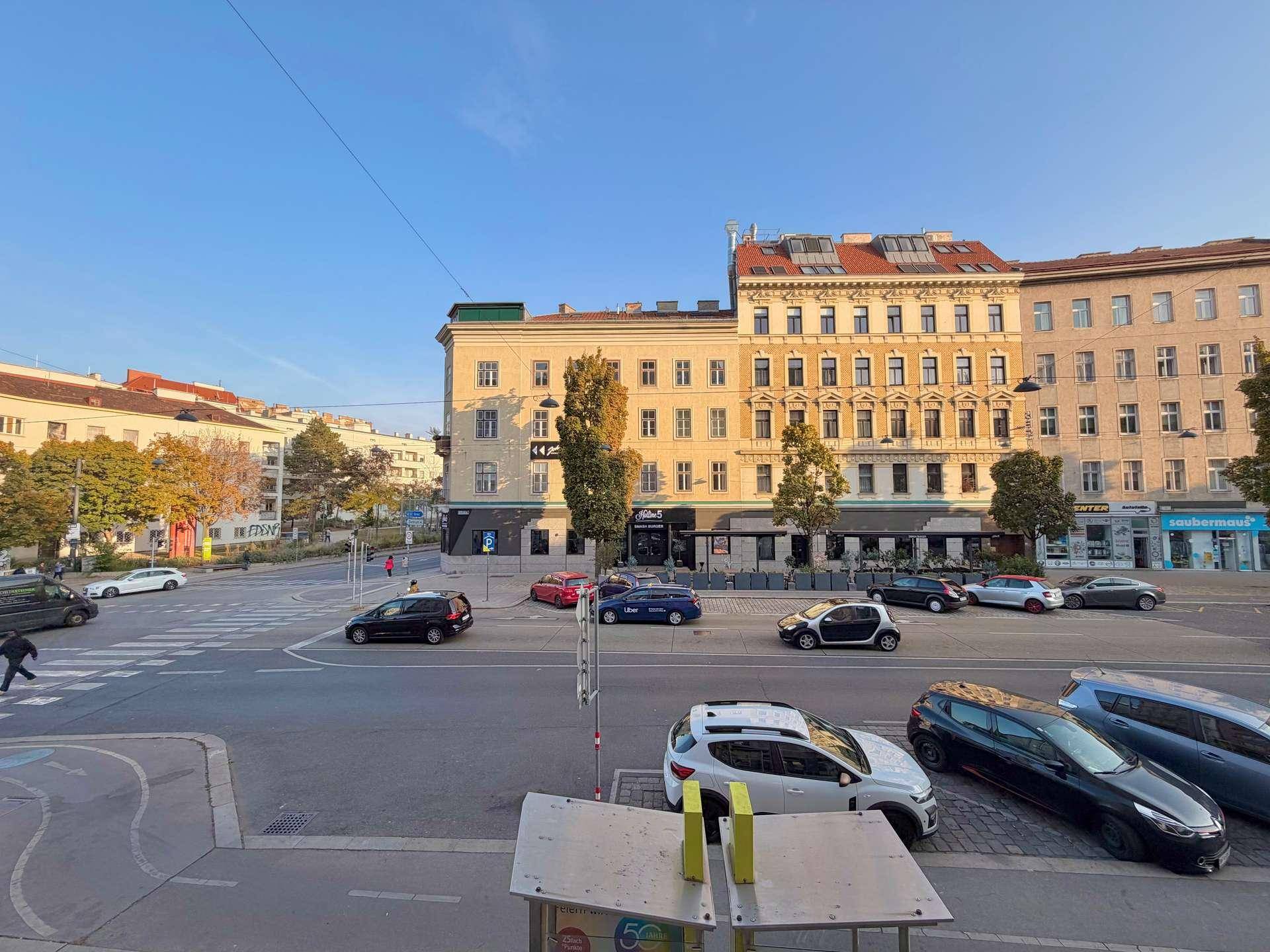 Weitläufiger Blick auf eine belebte Stadtkreuzung mit Gebäuden und Fahrzeugen.