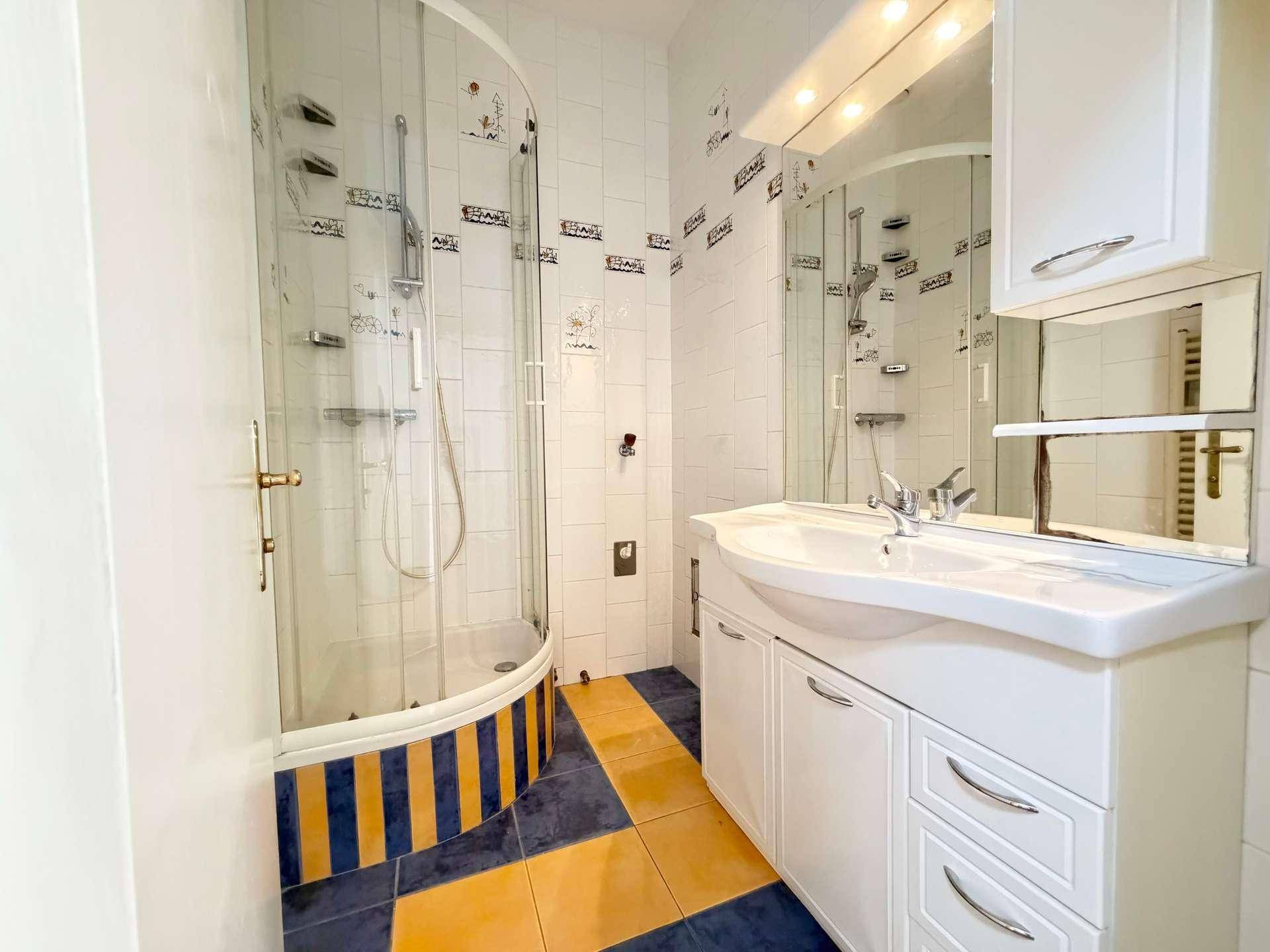 Badezimmer mit Duschkabine, Waschbecken und farbigen Fliesen in Blau und Gelb.