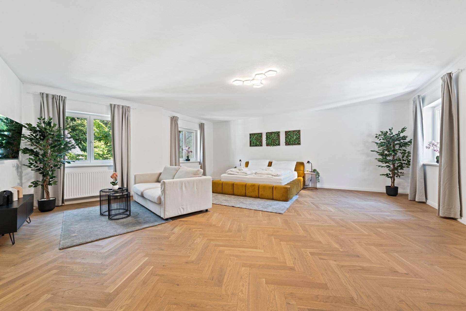 Geräumiges Schlafzimmer mit großem Bett, Sitzbereich und hellem Fischgrätparkett.