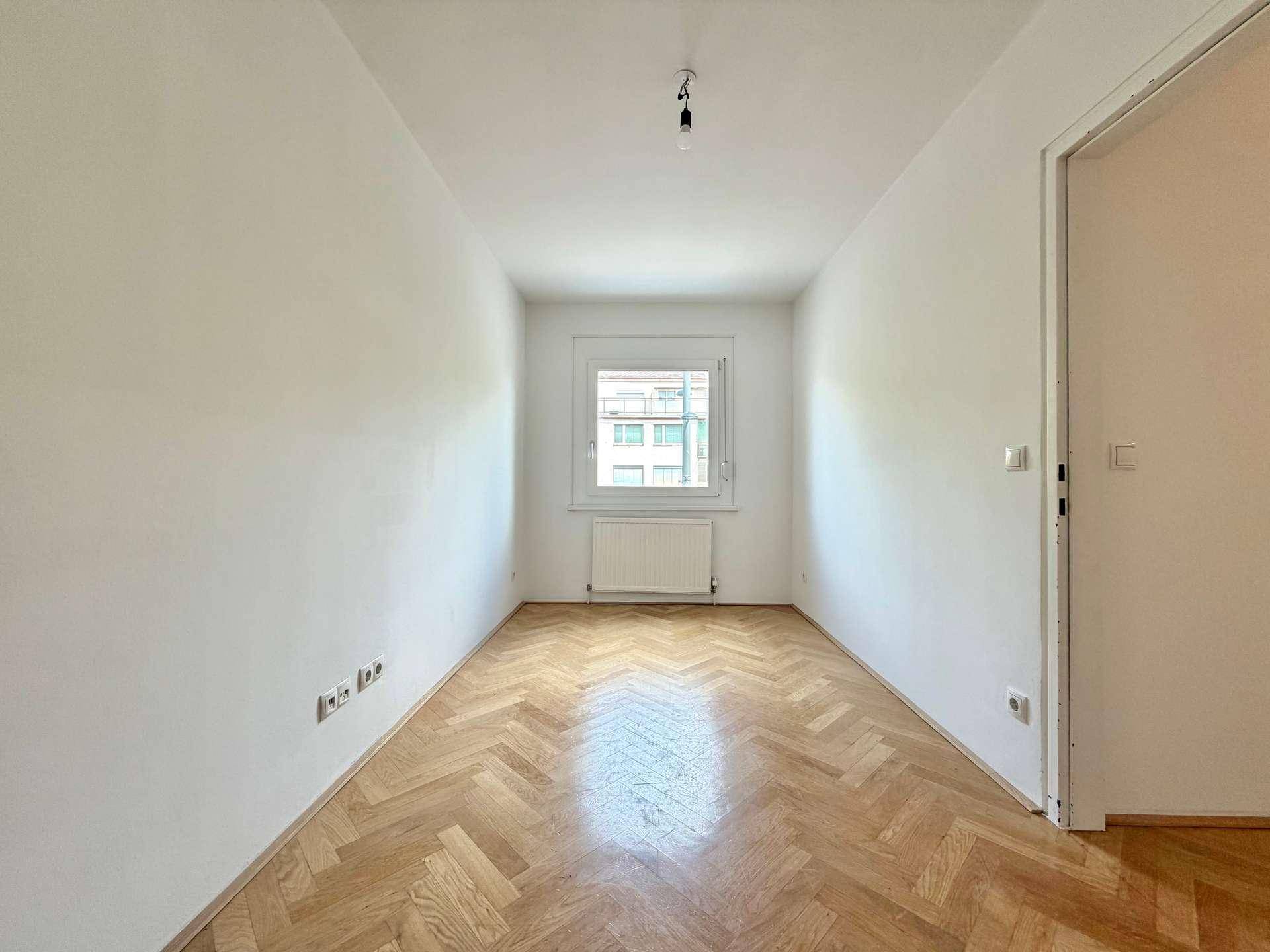 Ruhiges Zimmer mit Fischgrätparkettboden und einem Fenster, das viel Tageslicht hereinlässt.