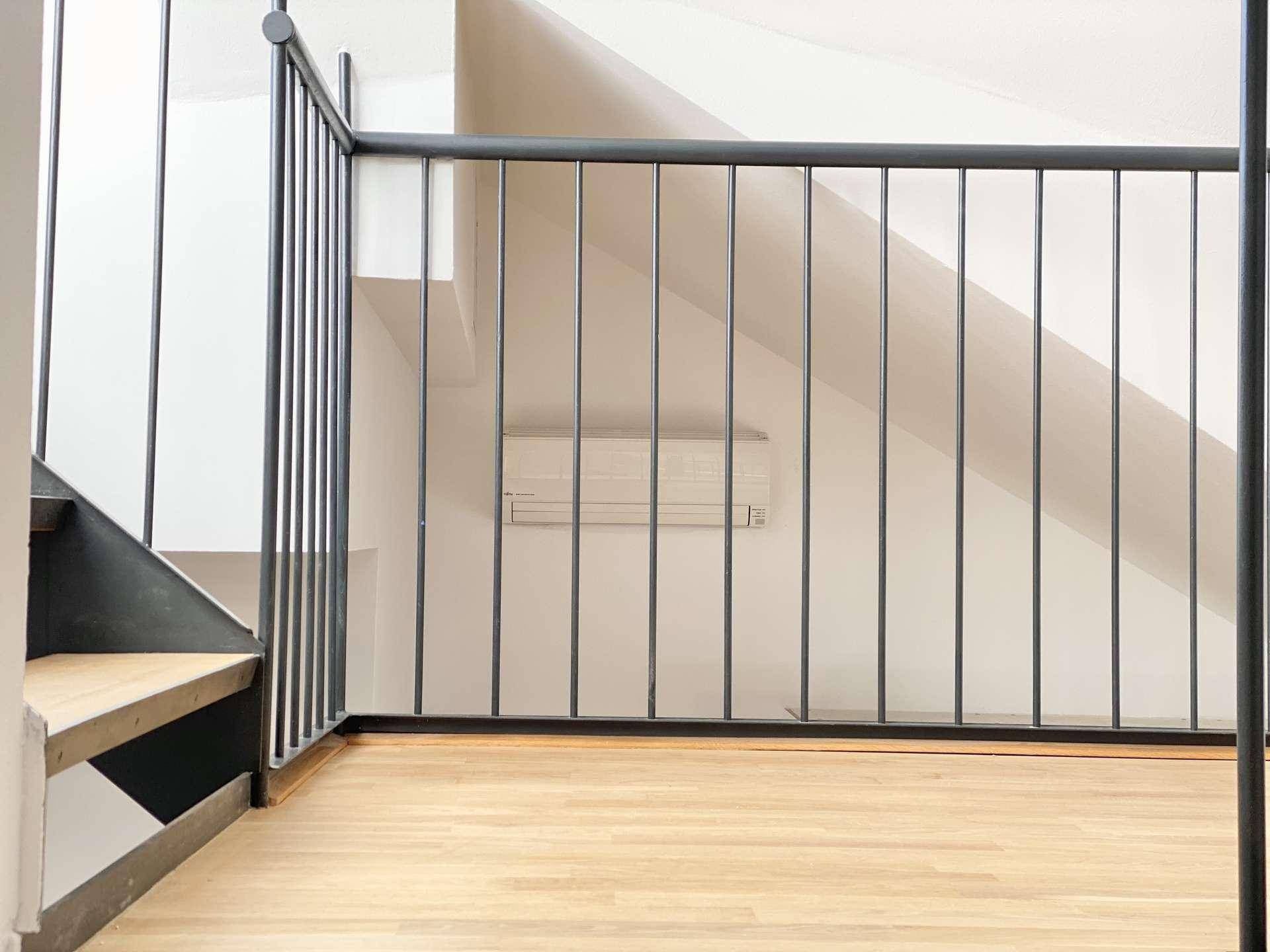 Oberer Treppenabsatz mit Holzboden, Metallgeländer und Klimaanlage an der Wand.