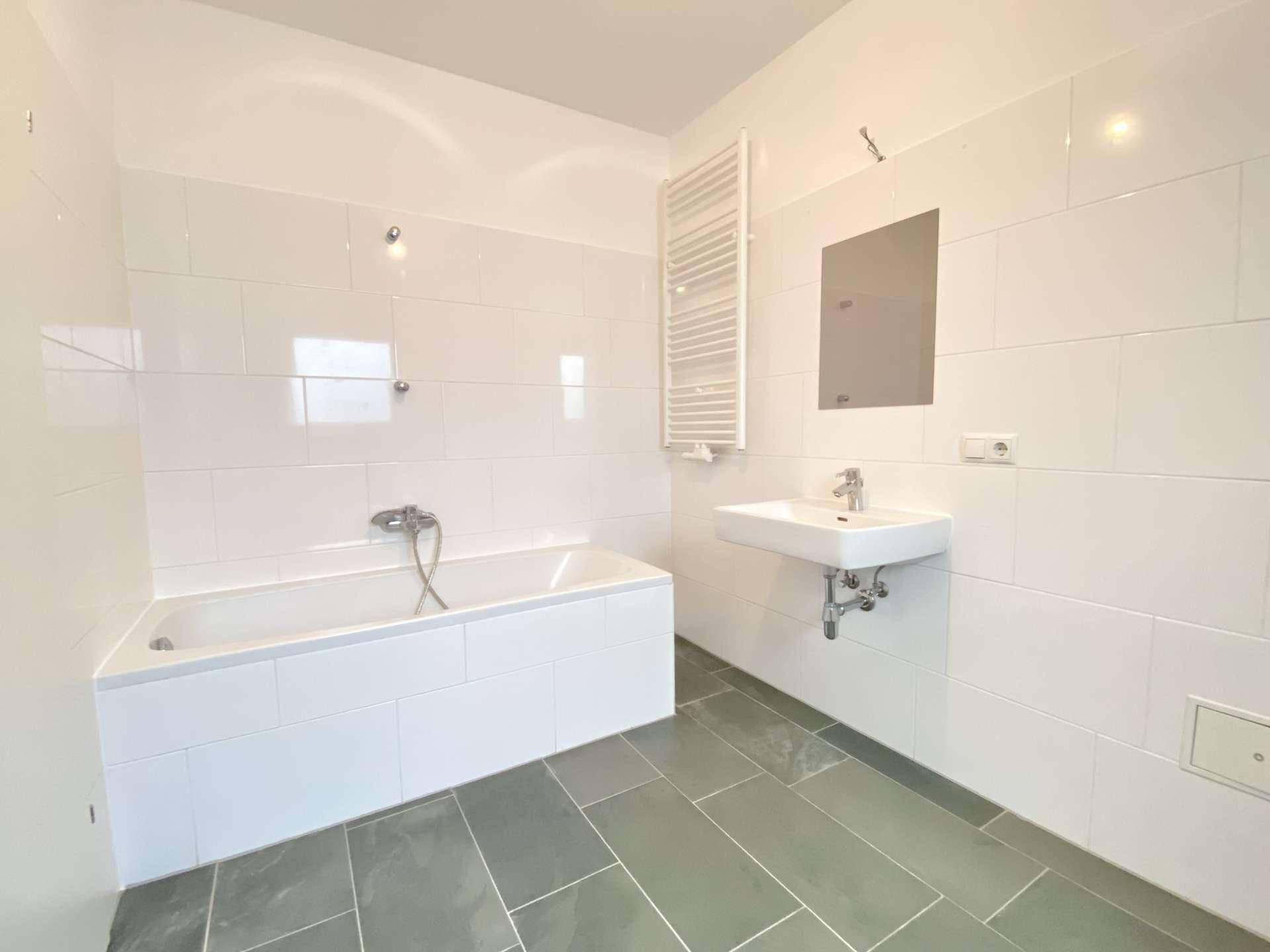 Helles Badezimmer mit Badewanne, Waschbecken und Handtuchheizkörper, komplett gefliest.