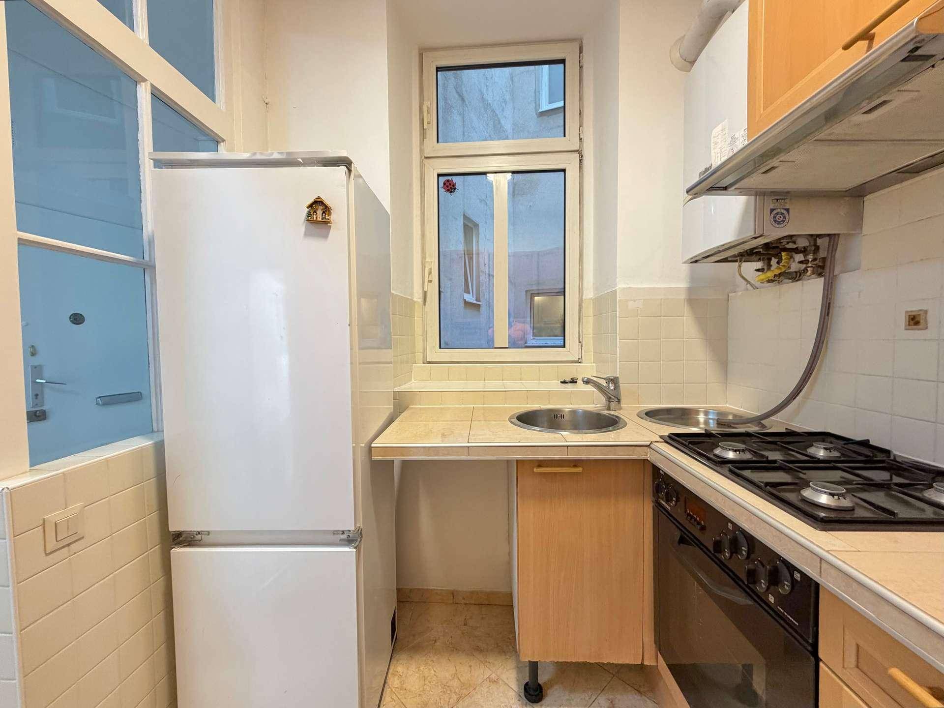 Kompakte Küche mit Fenster, Doppelspüle, Kühlschrank und Gasherd, ideal für kleine Haushalte.