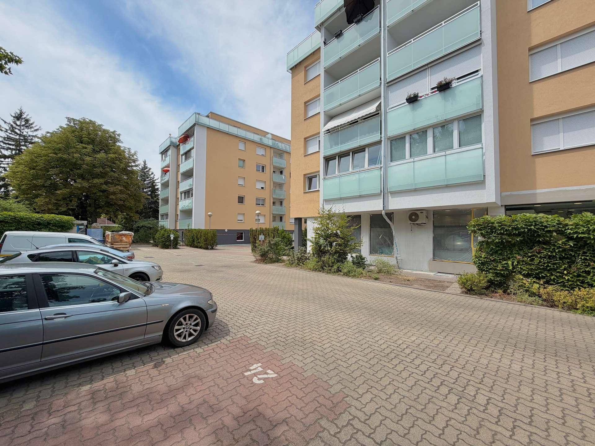 Außenansicht eines Wohnkomplexes mit Parkplätzen und begrünten Hecken.