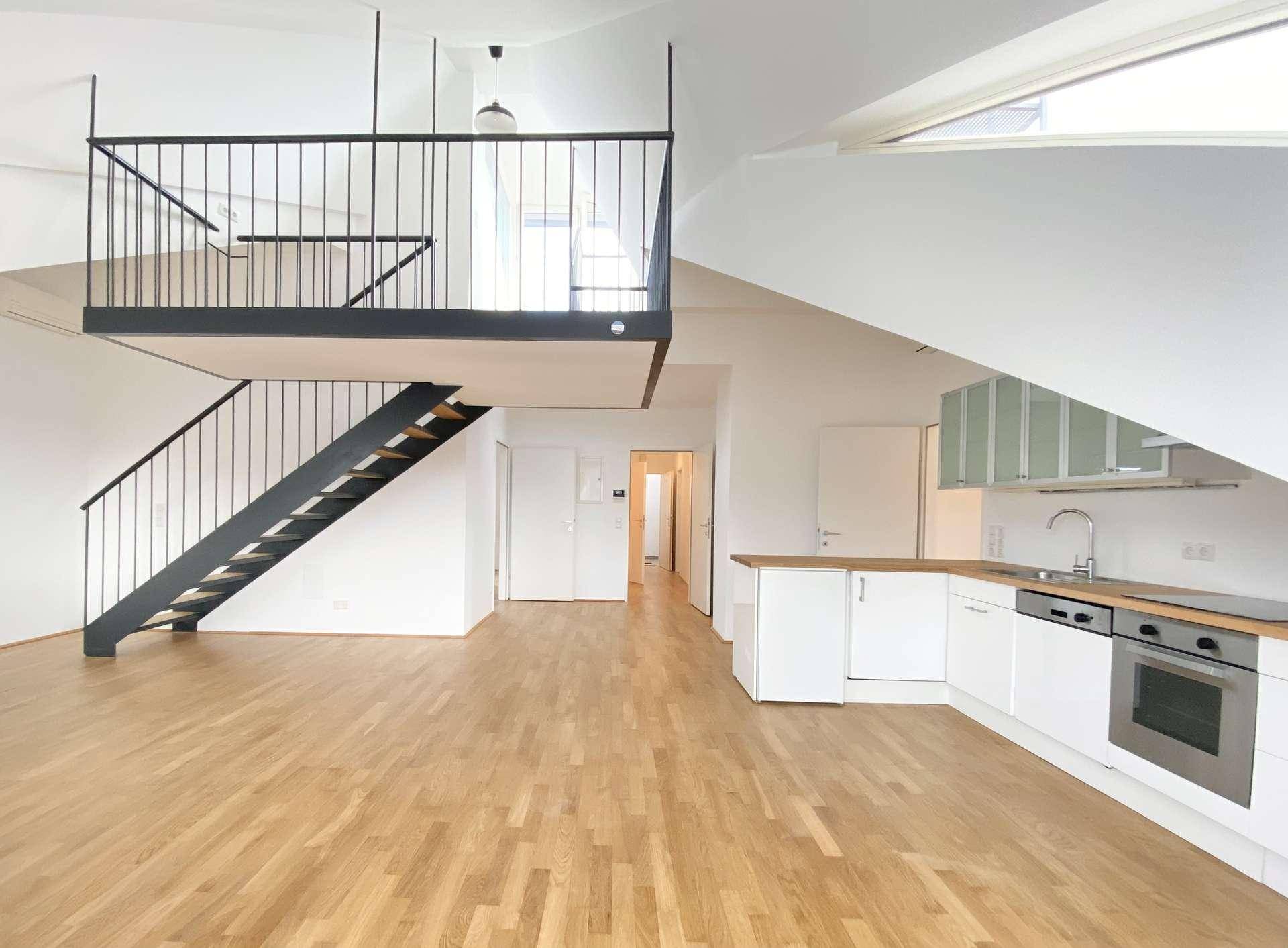 Offener Wohnbereich mit integrierter Küche, Holzfußboden und einer modernen Galerie mit Treppe.
