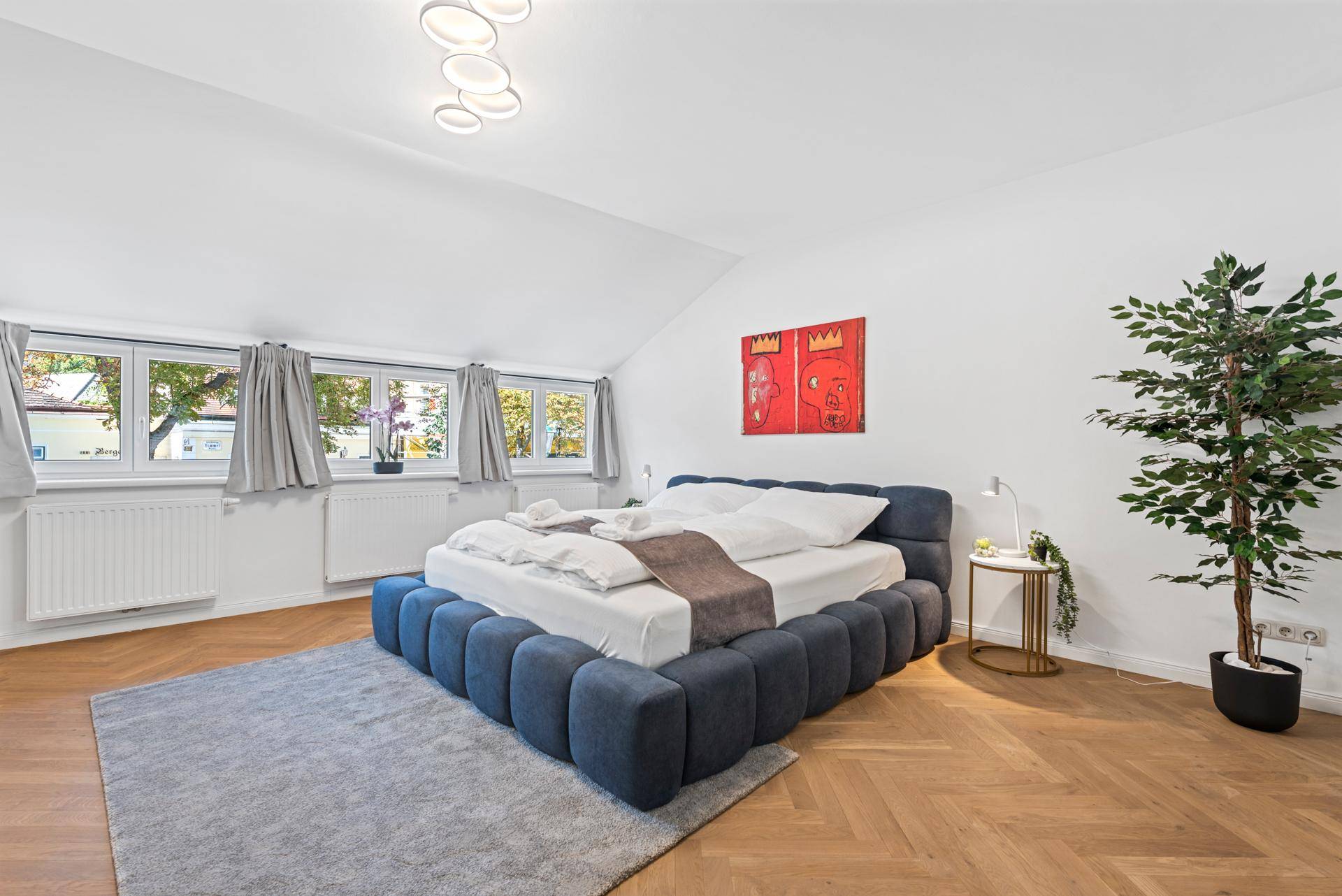Modernes Schlafzimmer im Dachgeschoss mit blauer Bettumrandung und großen Fenstern.
