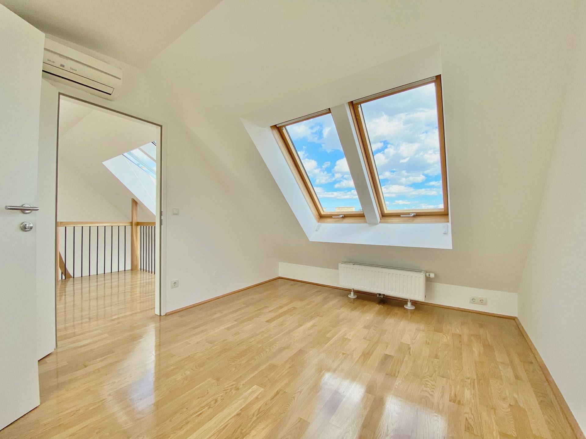 Helles Schlafzimmer mit Parkettboden und zwei Dachfenstern, die viel Licht spenden.