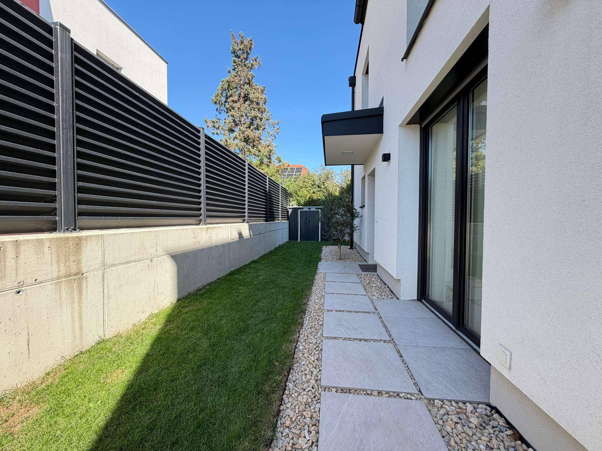 Seitlicher Gartenweg mit Trittplatten, Kies und Rasen entlang der Hausfassade.