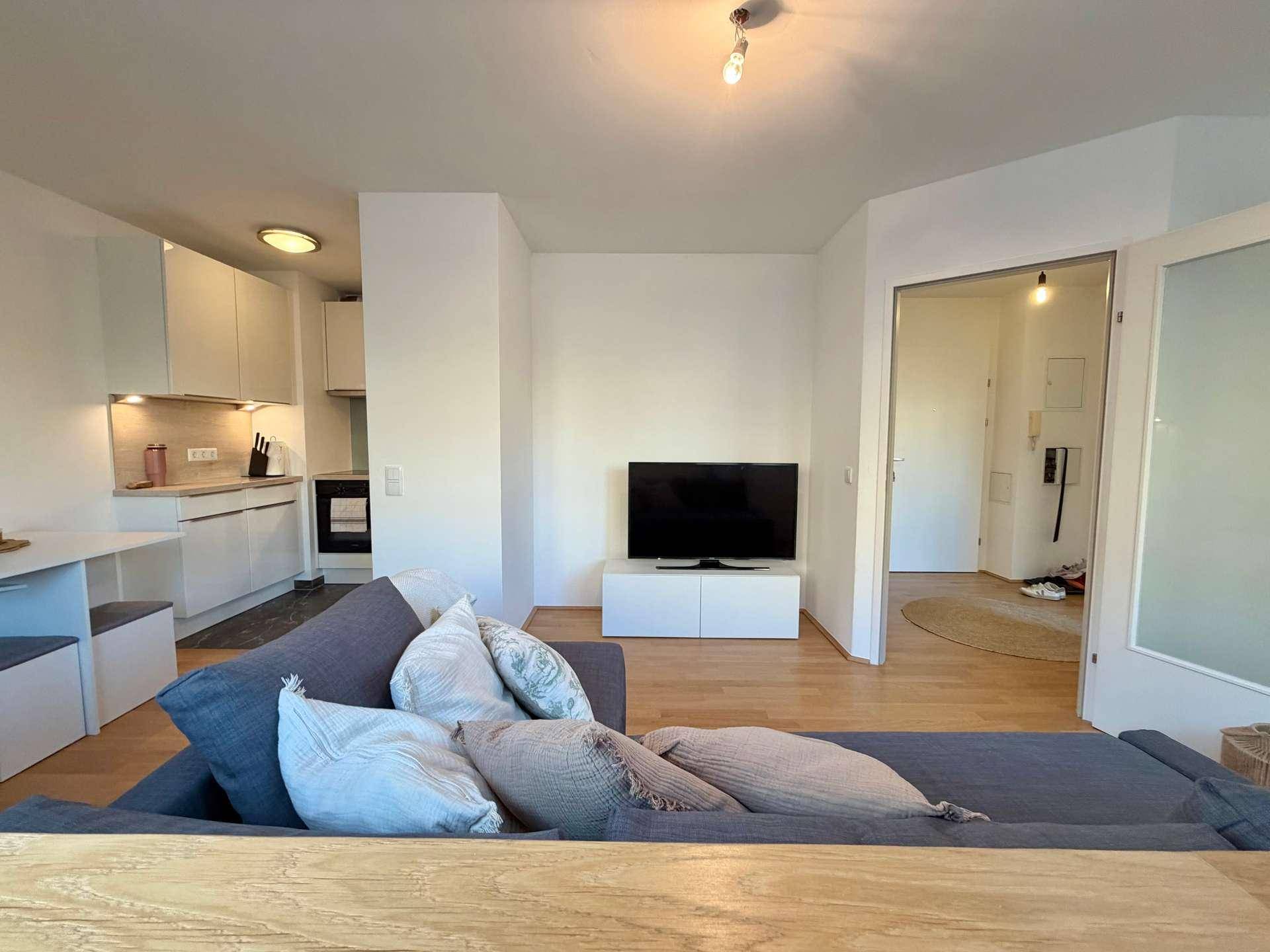 Offener Wohnbereich mit Sofa, Fernseher und angrenzender Küchenzeile.