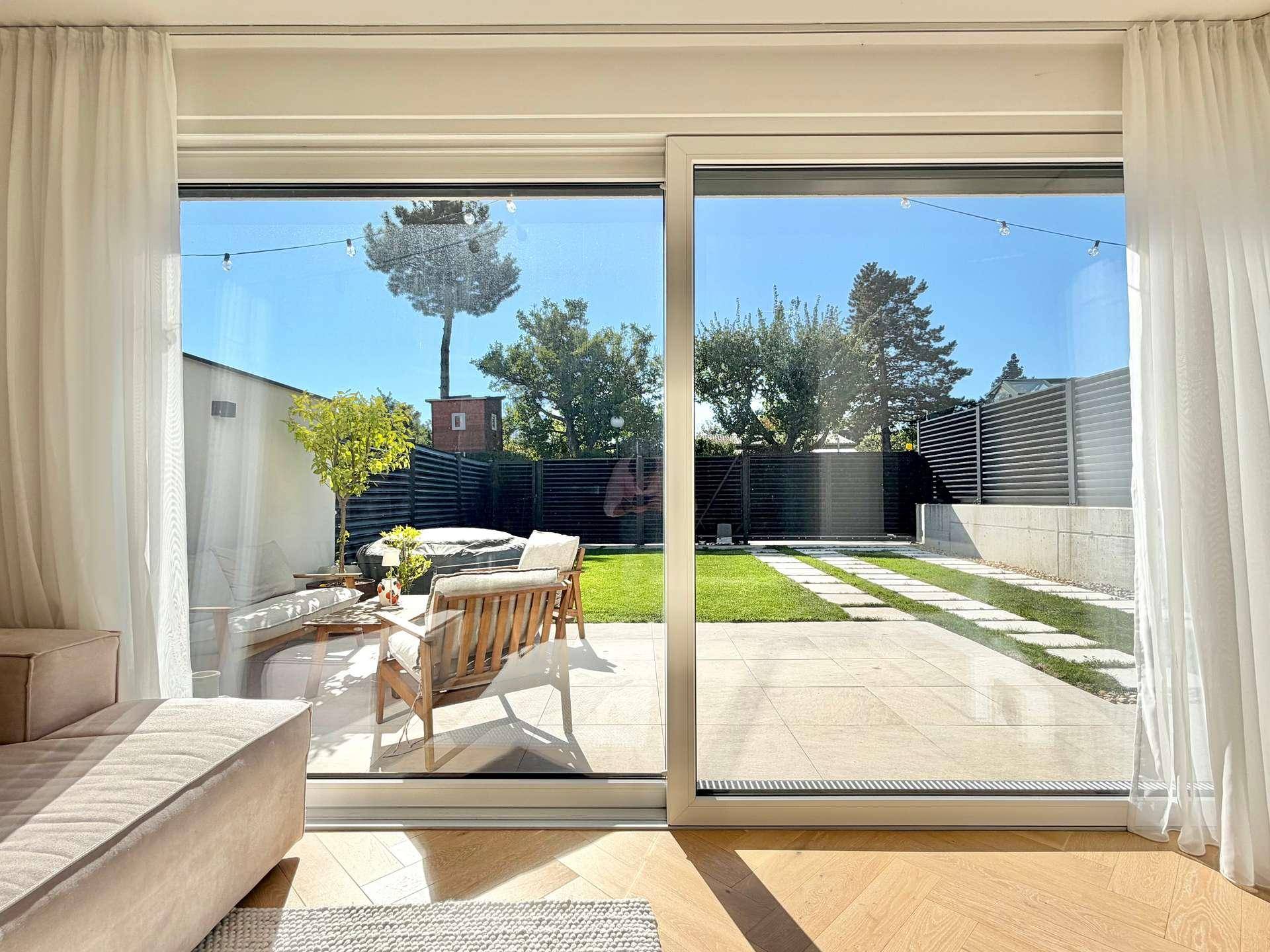 Weitläufiger Blick vom Wohnzimmer durch große Schiebetüren in den sonnigen Garten.