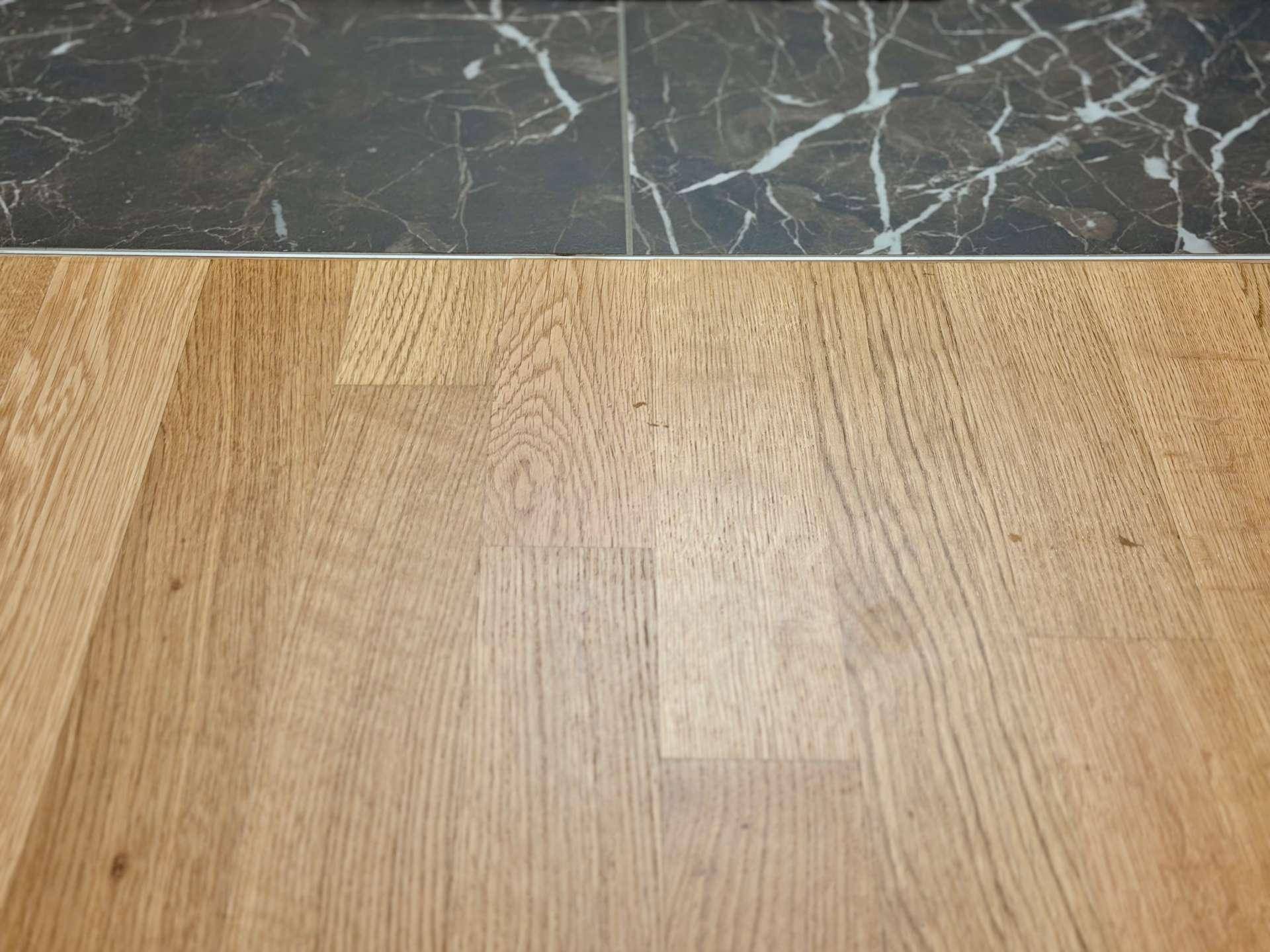 Übergang zwischen hellem Holzfußboden und dunklem Fliesenboden.