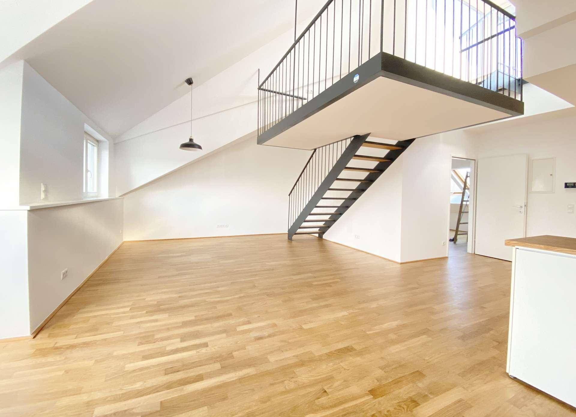 Geräumiger Wohnbereich mit Holzfußboden, viel Tageslicht und einer modernen Galerie mit Treppe.