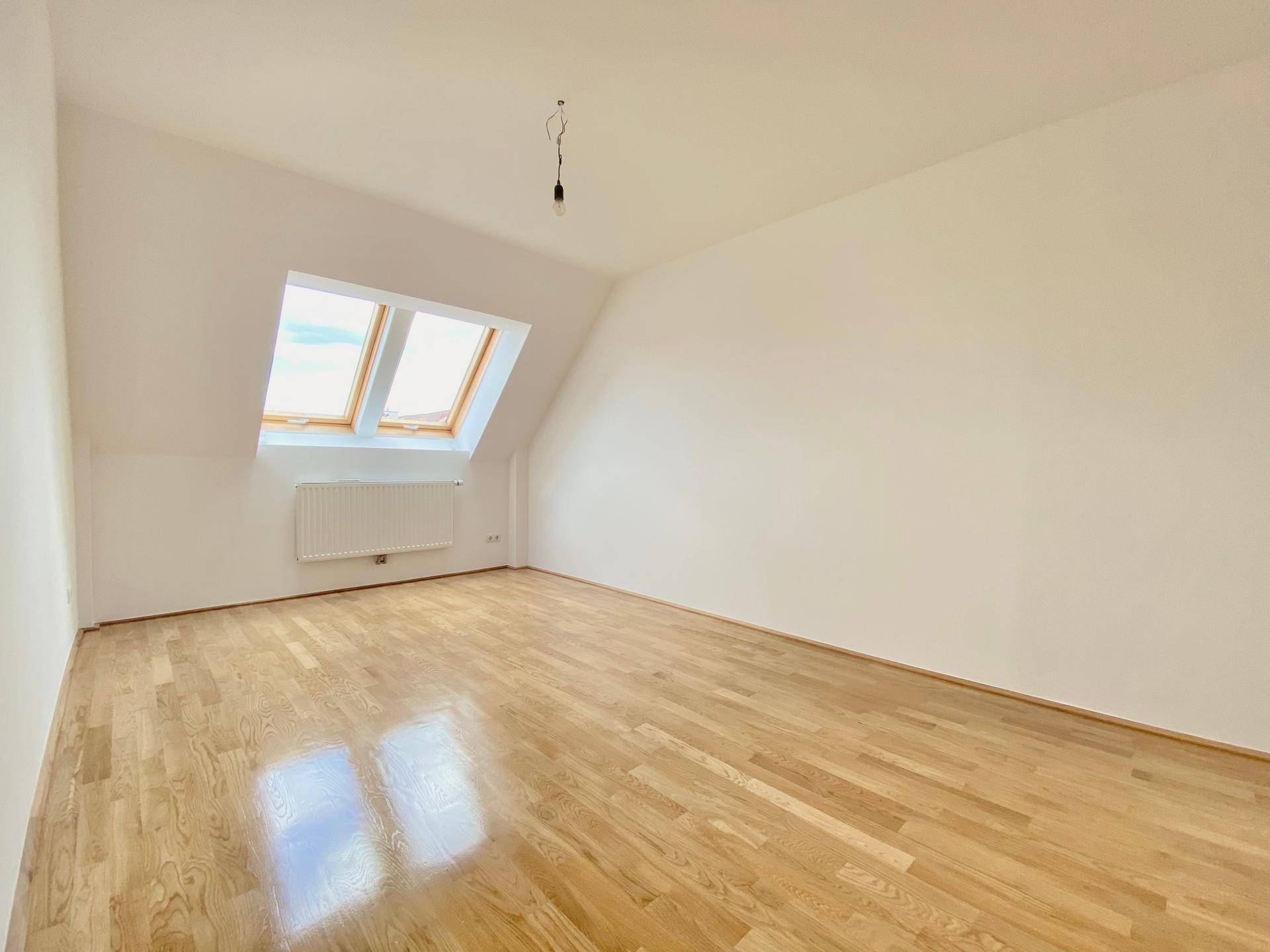 Helles Schlafzimmer mit Parkettboden und zwei Dachfenstern, die viel Licht spenden.