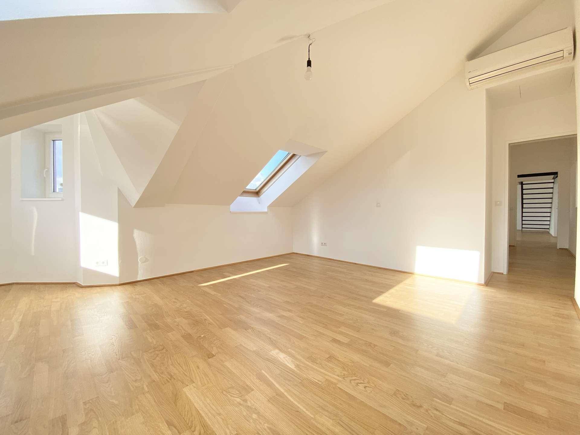 Helles Zimmer mit Holzfußboden, schrägen Wänden, Dachfenster und Klimaanlage.