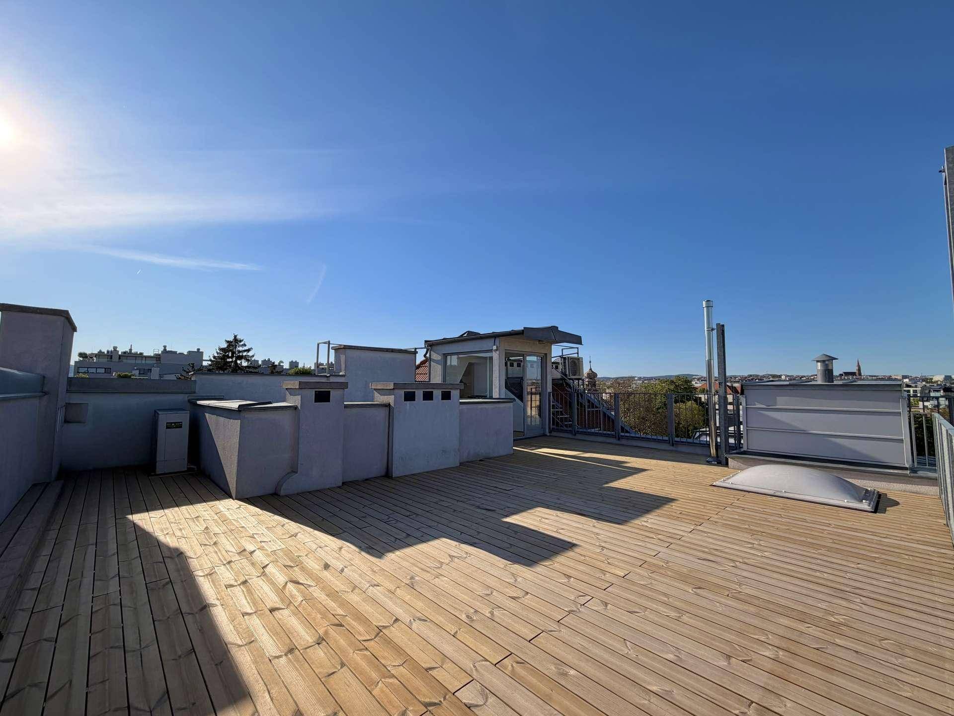 Sonnige Dachterrasse mit Holzboden und weitem Blick über die Dächer der Stadt.