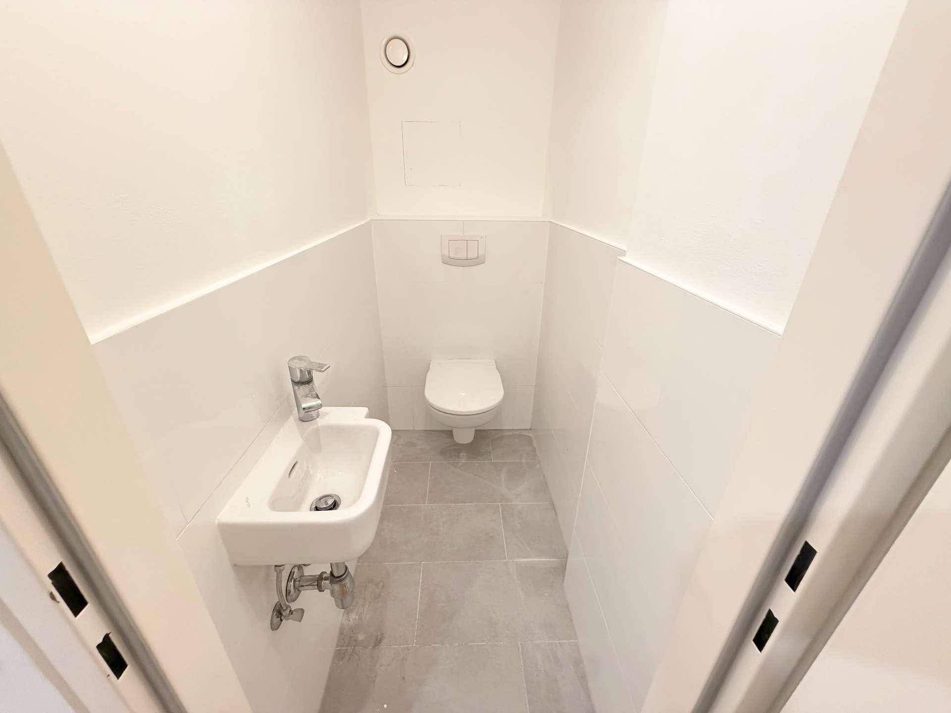 Separates Gäste-WC mit wandhängender Toilette, kleinem Waschbecken und modernen Fliesen.