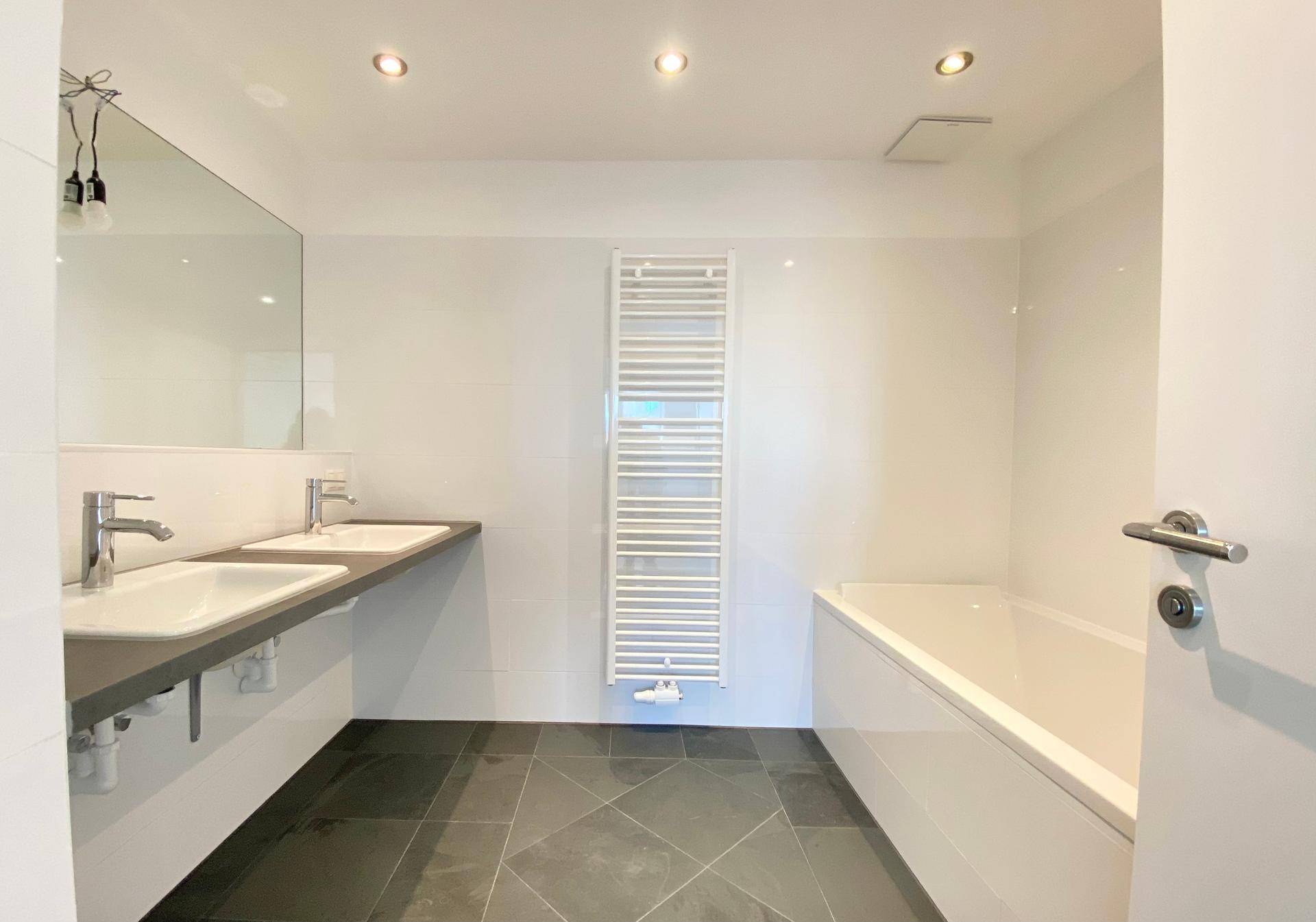 Modernes Badezimmer mit Doppelwaschbecken, Badewanne und beheiztem Handtuchhalter.
