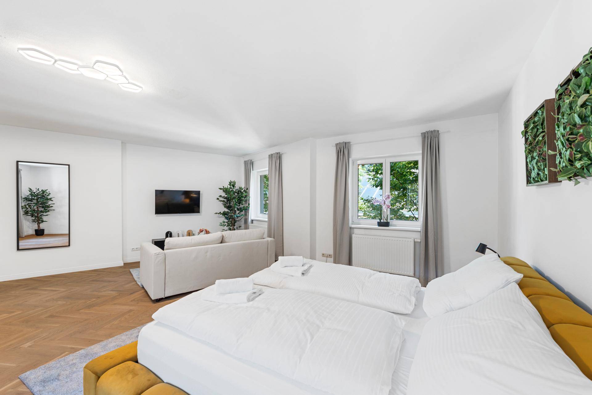 Komfortables Schlafzimmer mit Doppelbett, Sofa und Blick ins Grüne durch die Fenster.