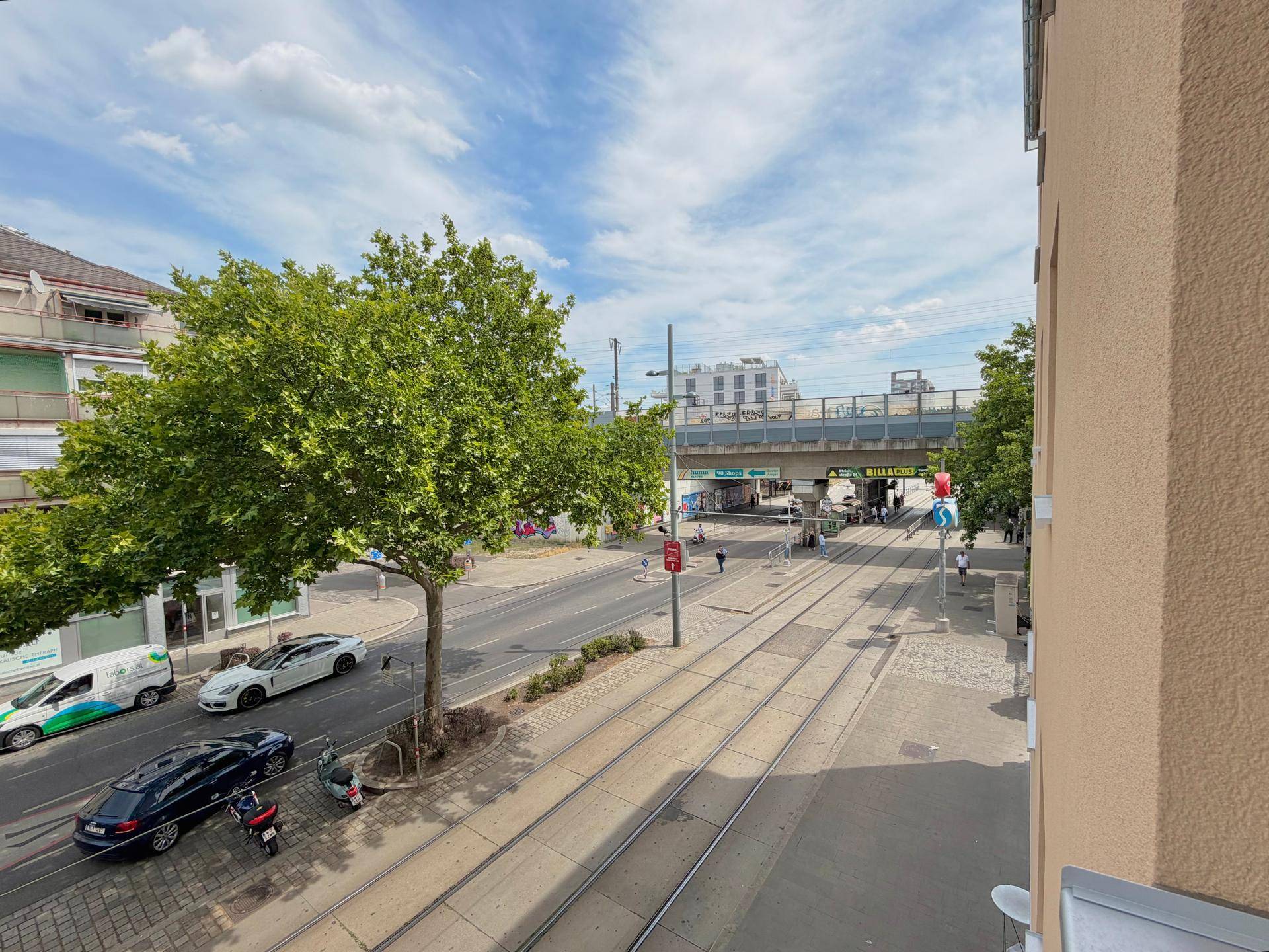 Panoramablick auf eine städtische Straße mit Verkehr, Bäumen und Straßenbahnschienen.