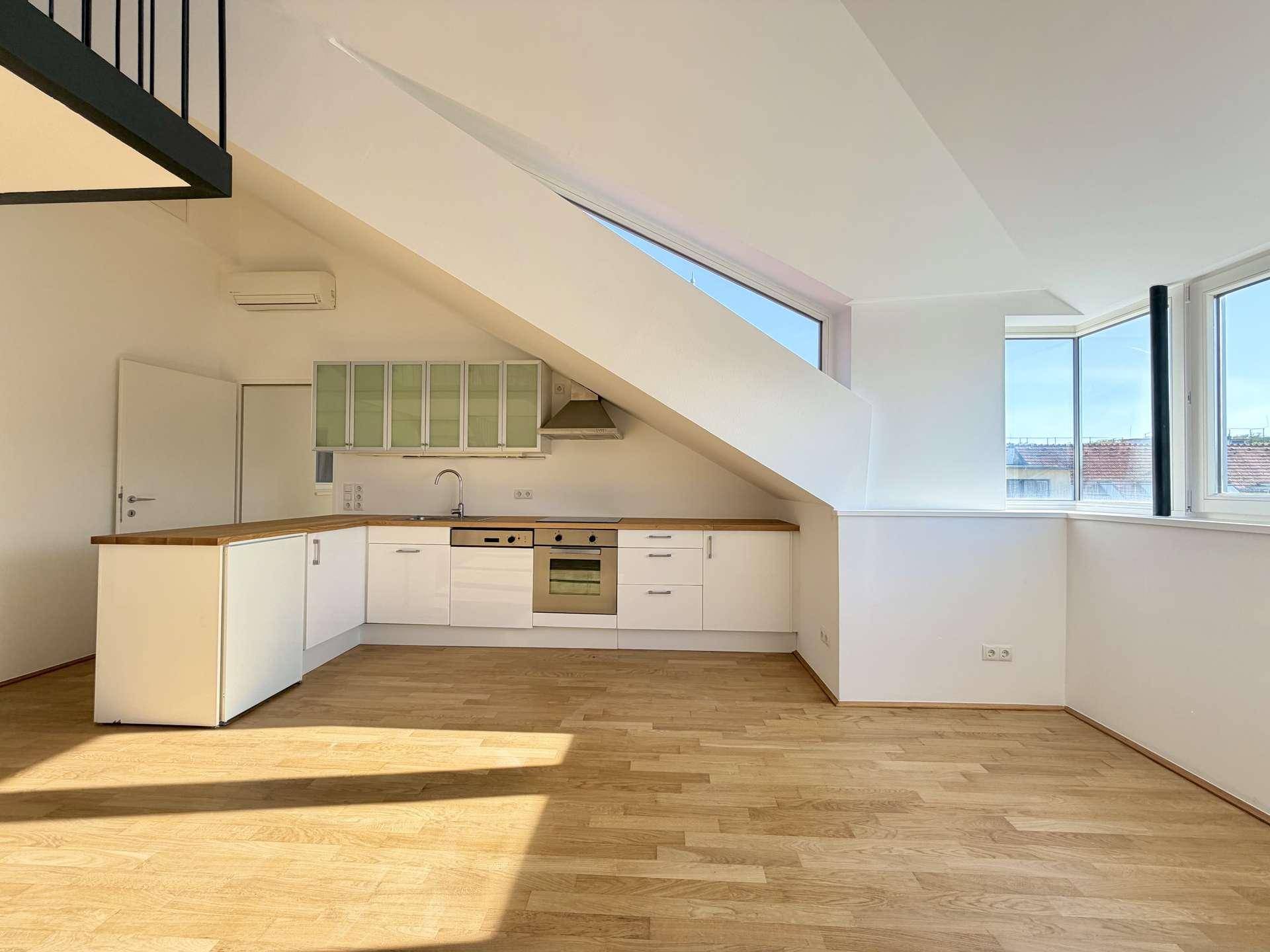 Moderne Einbauküche mit Holz-Arbeitsplatte, weißen Schränken und viel Tageslicht durch große Fenster.