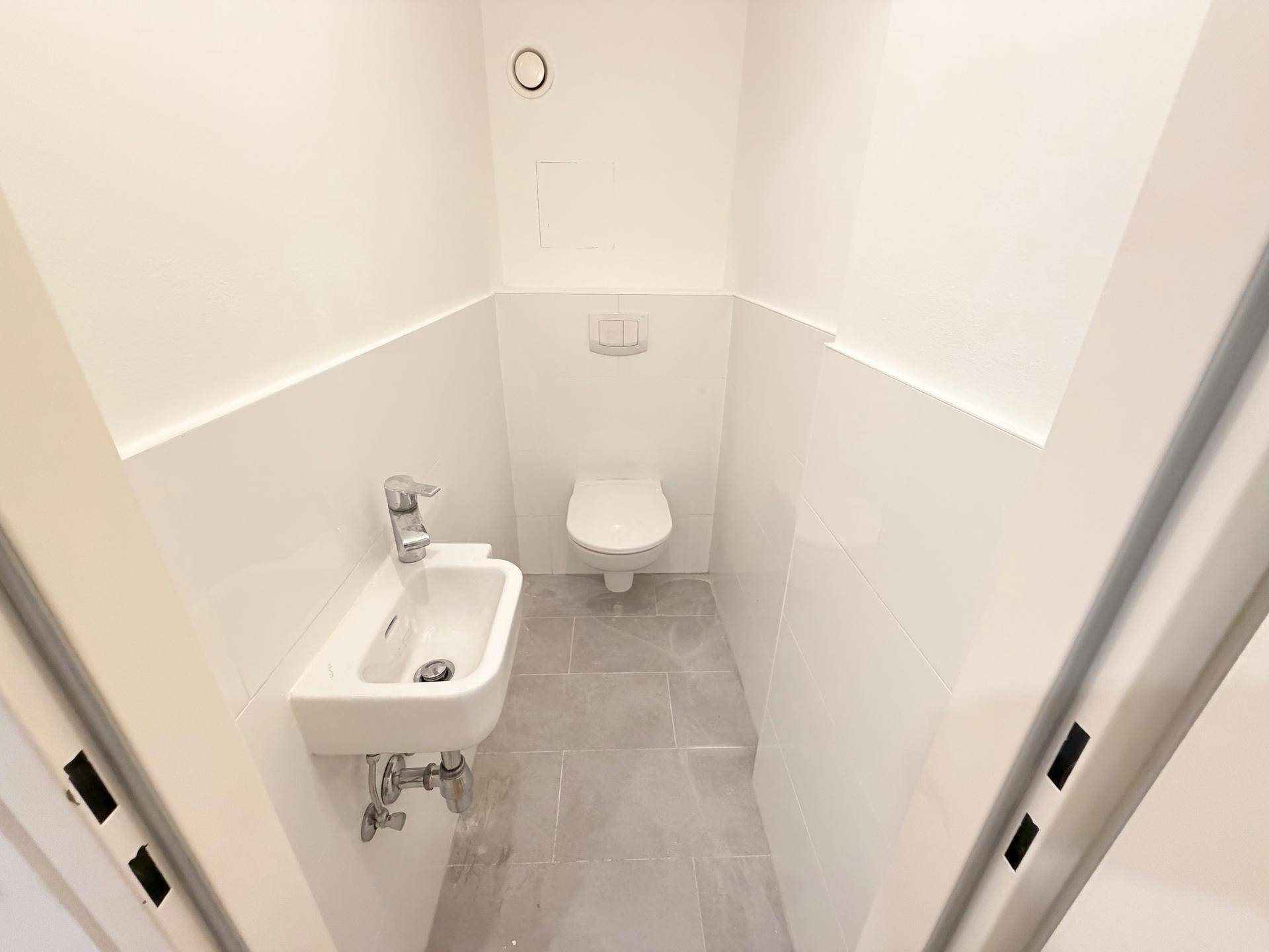 Modernes Gäste-WC mit wandhängendem WC, kleinem Waschbecken und hellen Fliesen.