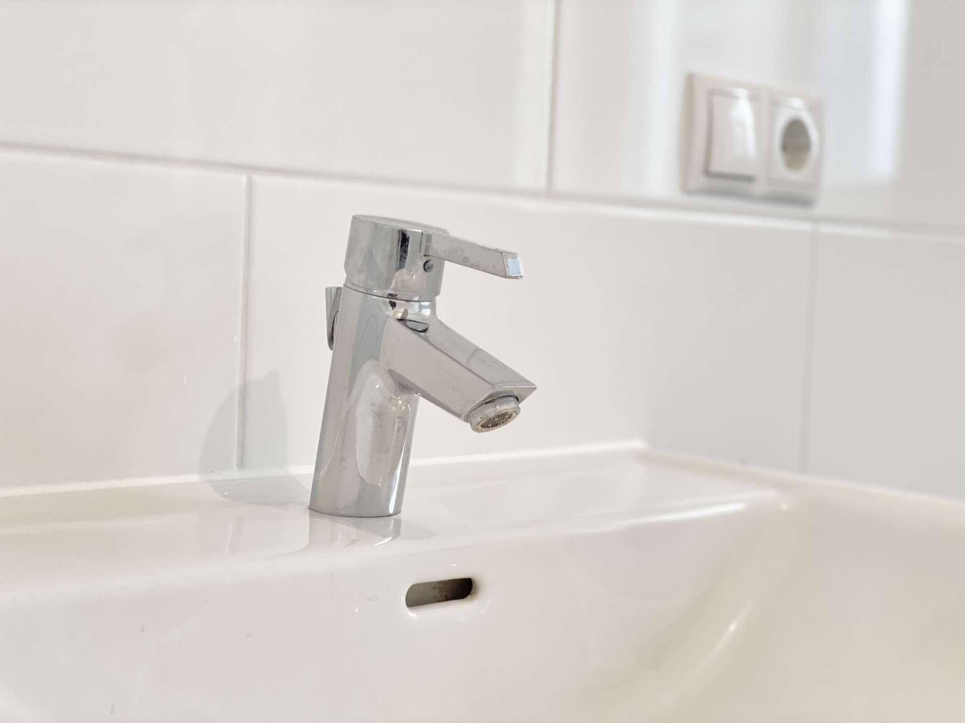 Detailansicht eines modernen Chromwasserhahns auf einem weißen Waschbecken.