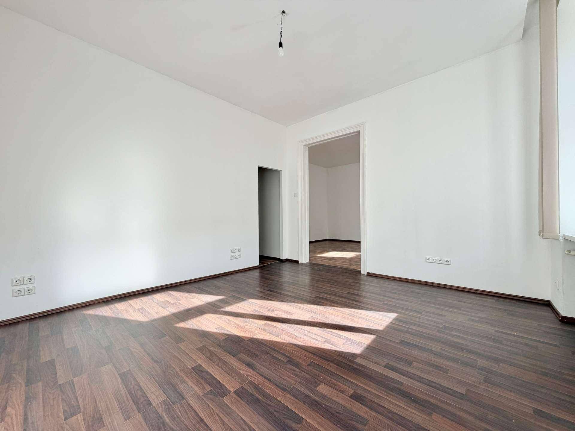 Wohnzimmer mit Laminatboden und weiß gestrichenen Wänden, bereit für individuelle Gestaltung.