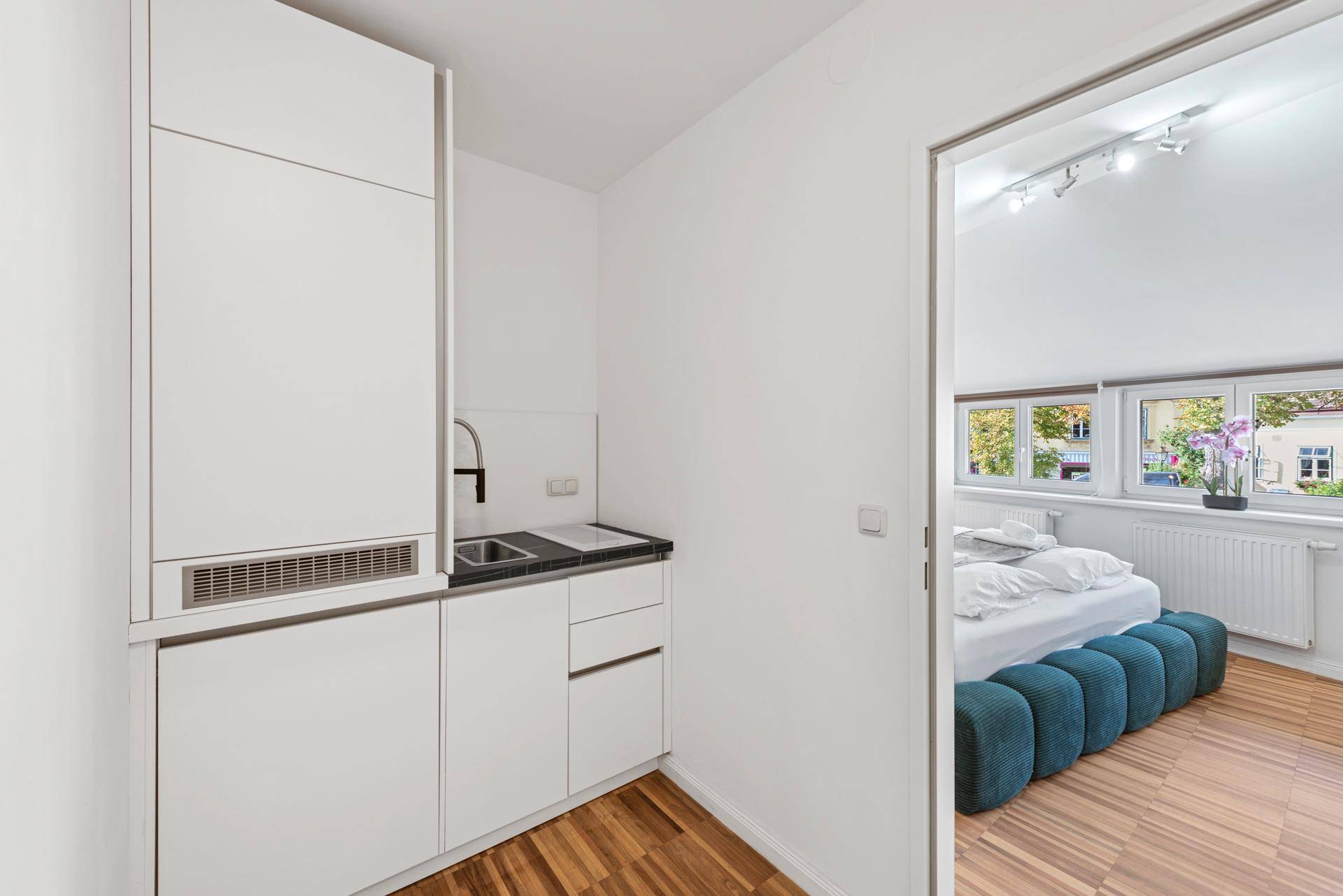Kleine, funktionale Küchenzeile mit Spüle und Kochfeld, angrenzend an ein Schlafzimmer.