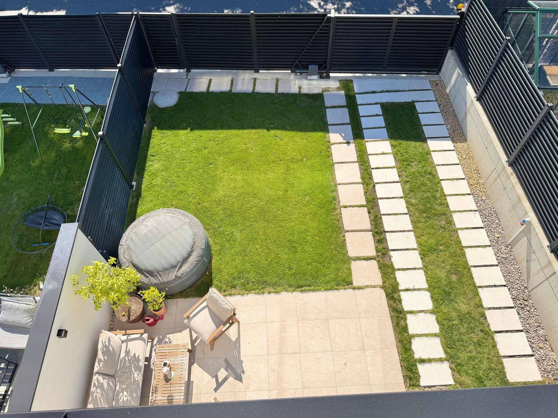 Gepflegter Garten mit Rasenfläche, Trittsteinen, Terrasse und Whirlpool.