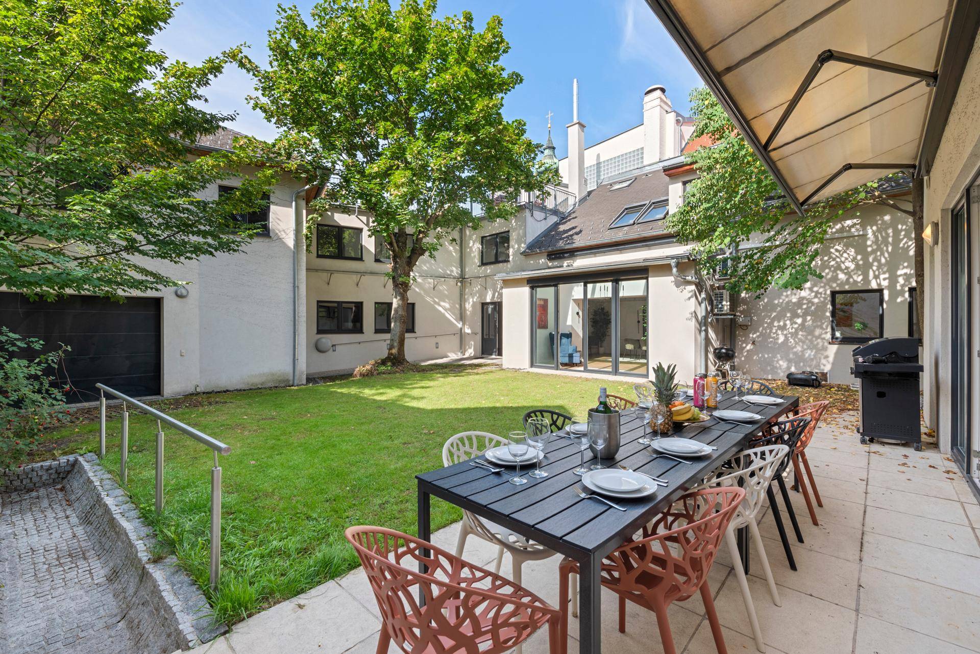 Große Terrasse mit Esstisch und Grillbereich, angrenzend an einen gepflegten Garten.
