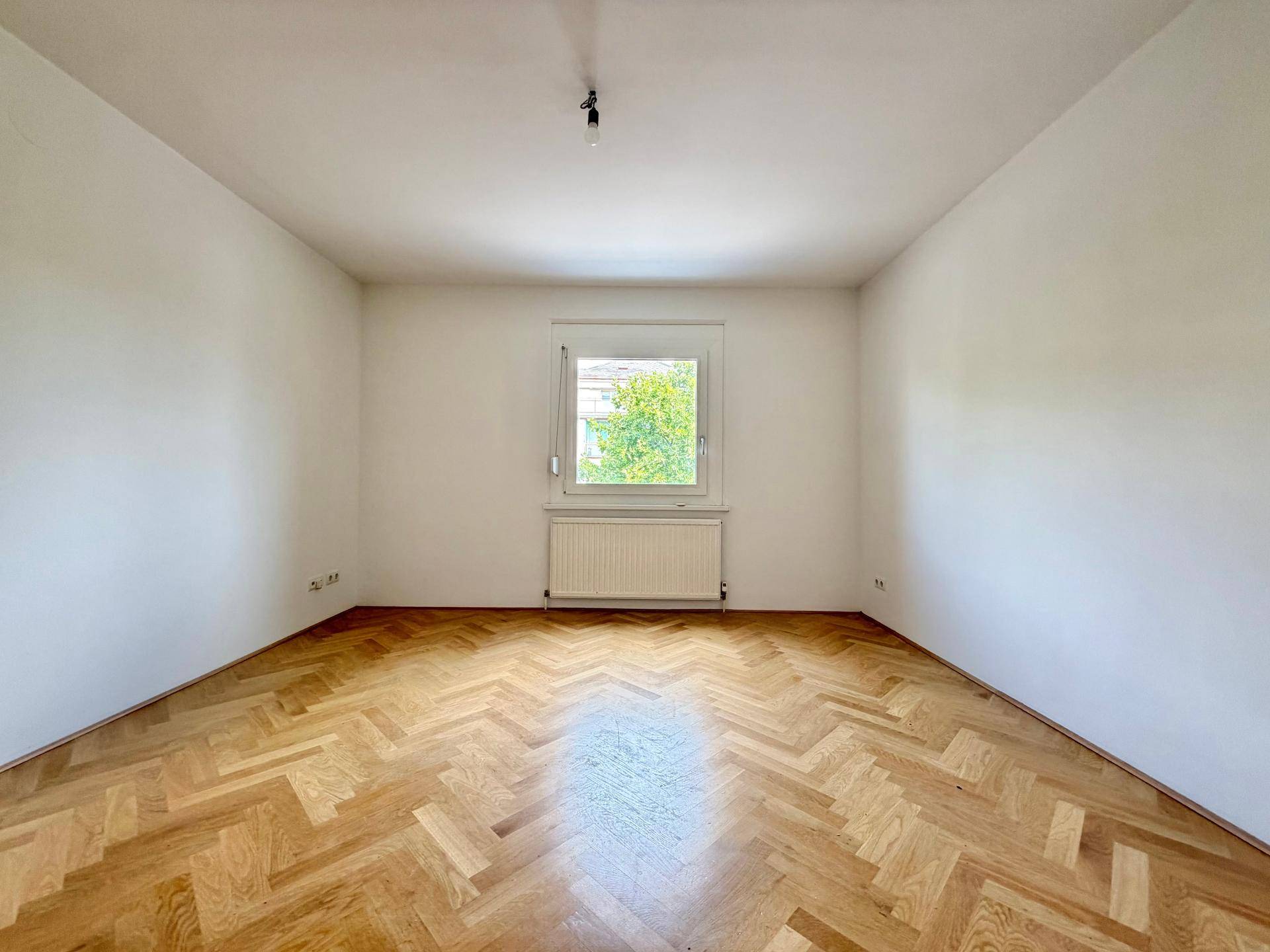 Geräumiges Zimmer mit Fischgrätparkett und Blick ins Grüne, das Ruhe und Helligkeit bietet.