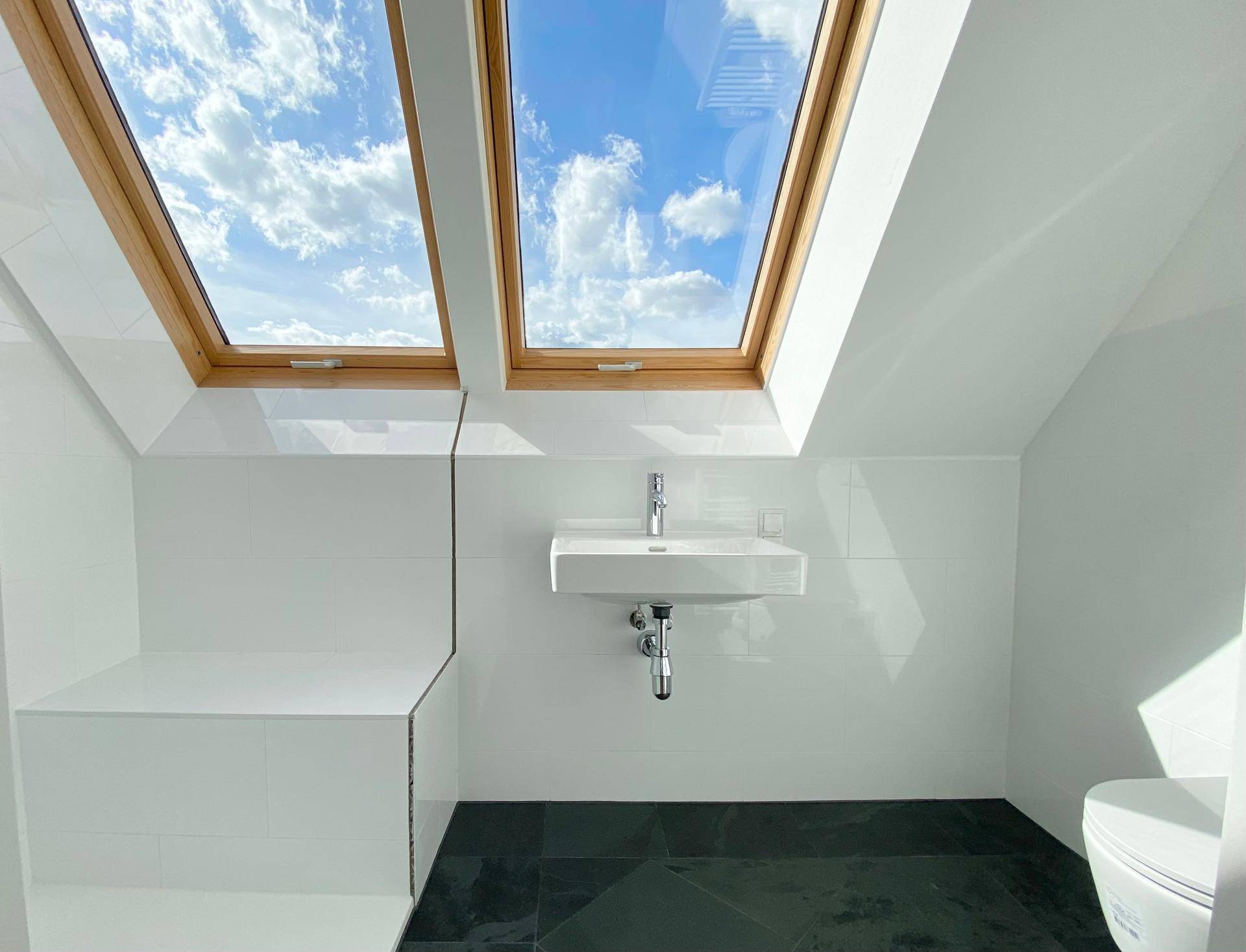 Modernes Badezimmer mit Waschbecken, Duschbereich und Dachfenster für Tageslicht.