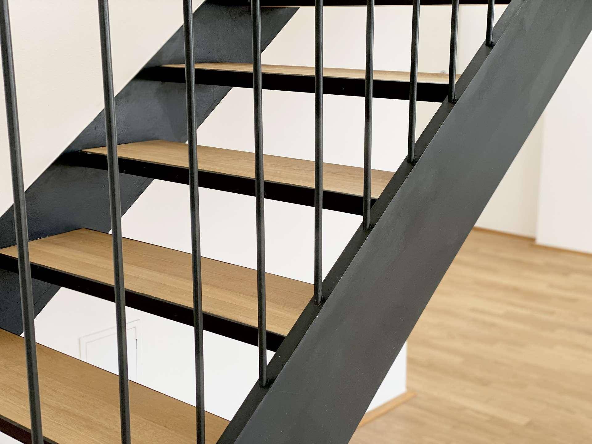 Detailansicht der modernen Treppe mit Holzstufen und schwarzem Metallgeländer.