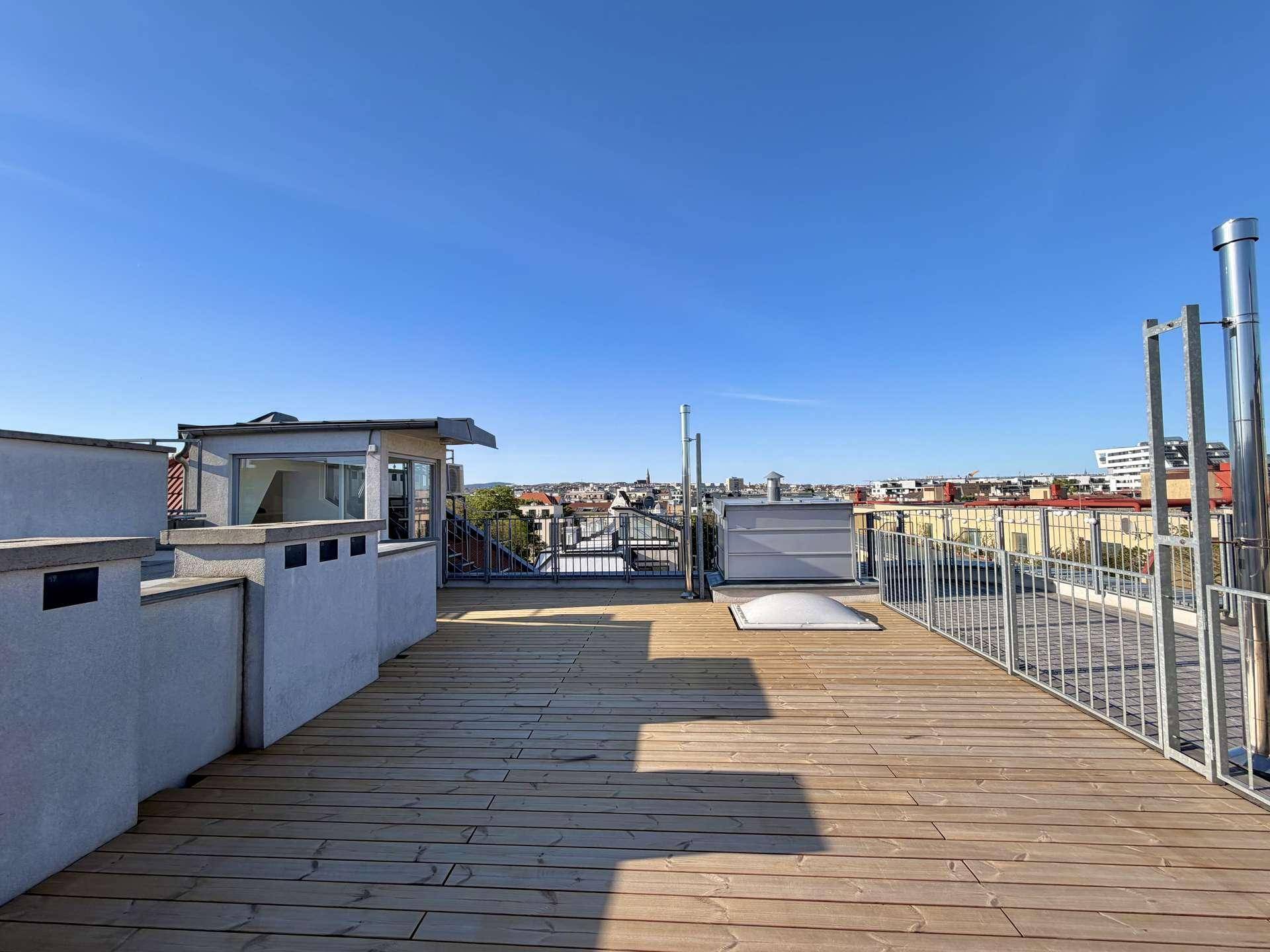 Weitläufige Dachterrasse mit Holzboden und Panoramablick über die Stadt unter blauem Himmel.