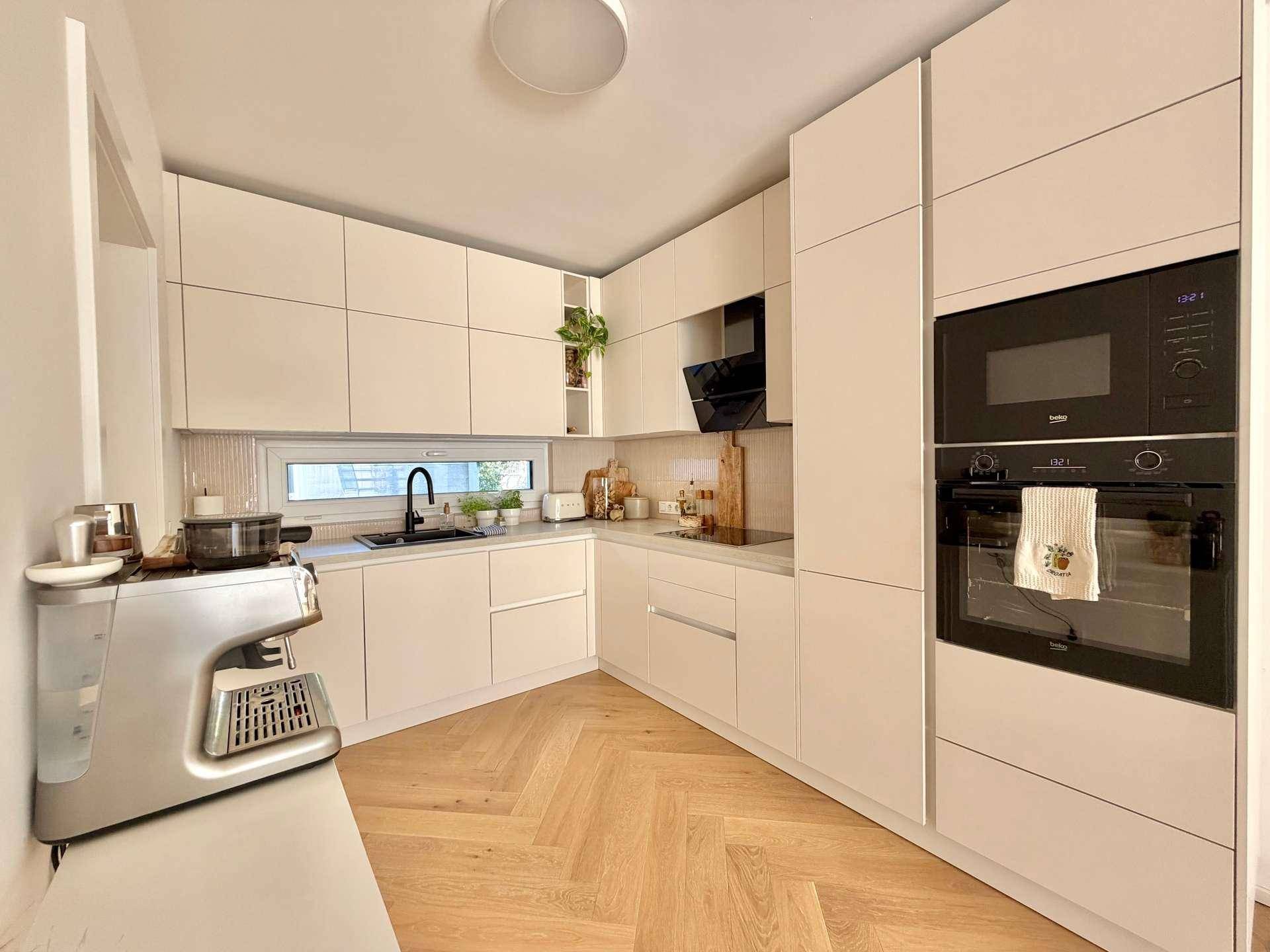 Helle, moderne Küche mit weißen Fronten, Einbaugeräten und Holzboden in Fischgrätmuster.