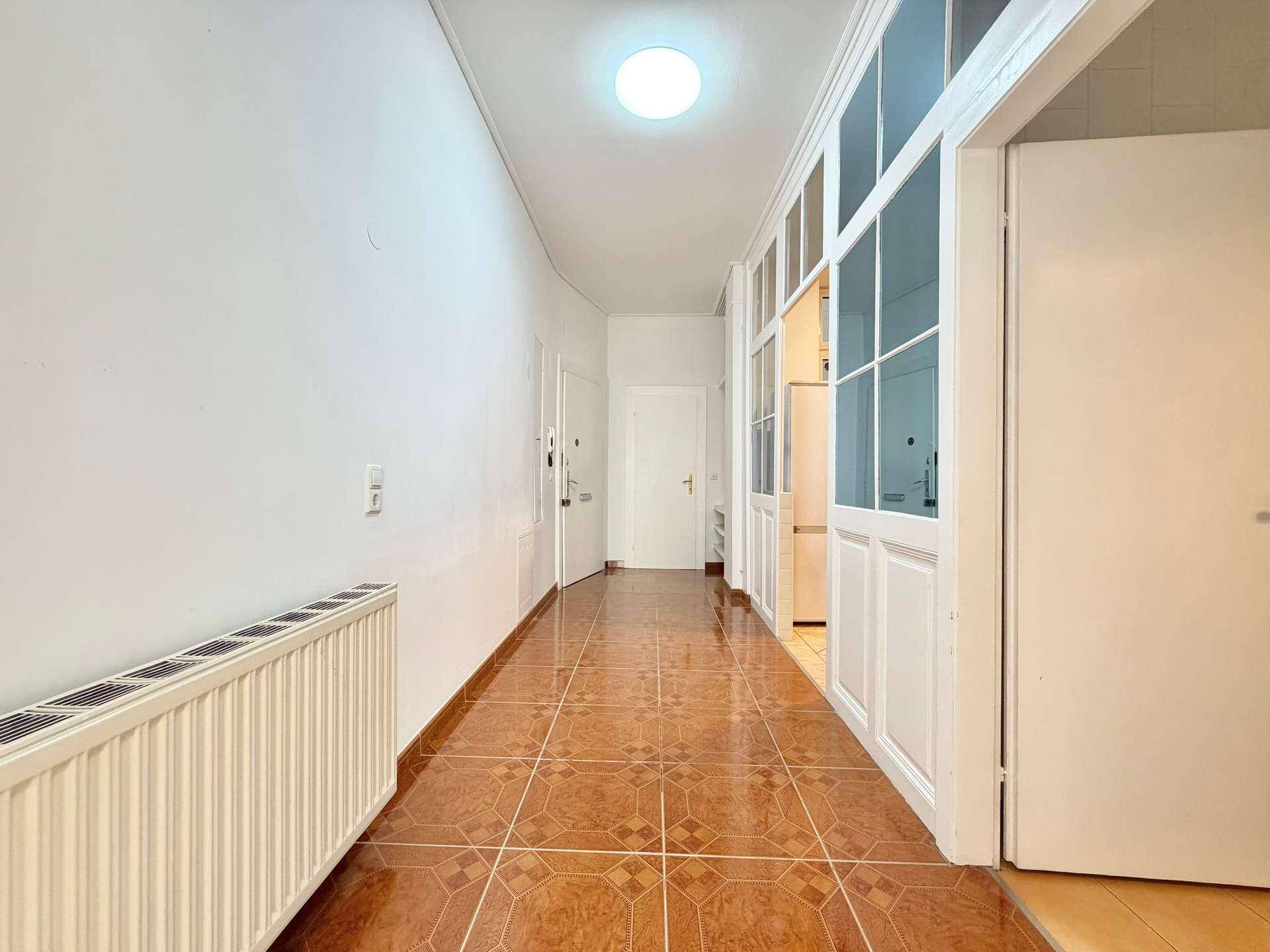Langer Flur mit Terrakotta-Fliesenboden, Heizkörper und Zugang zu verschiedenen Räumen.