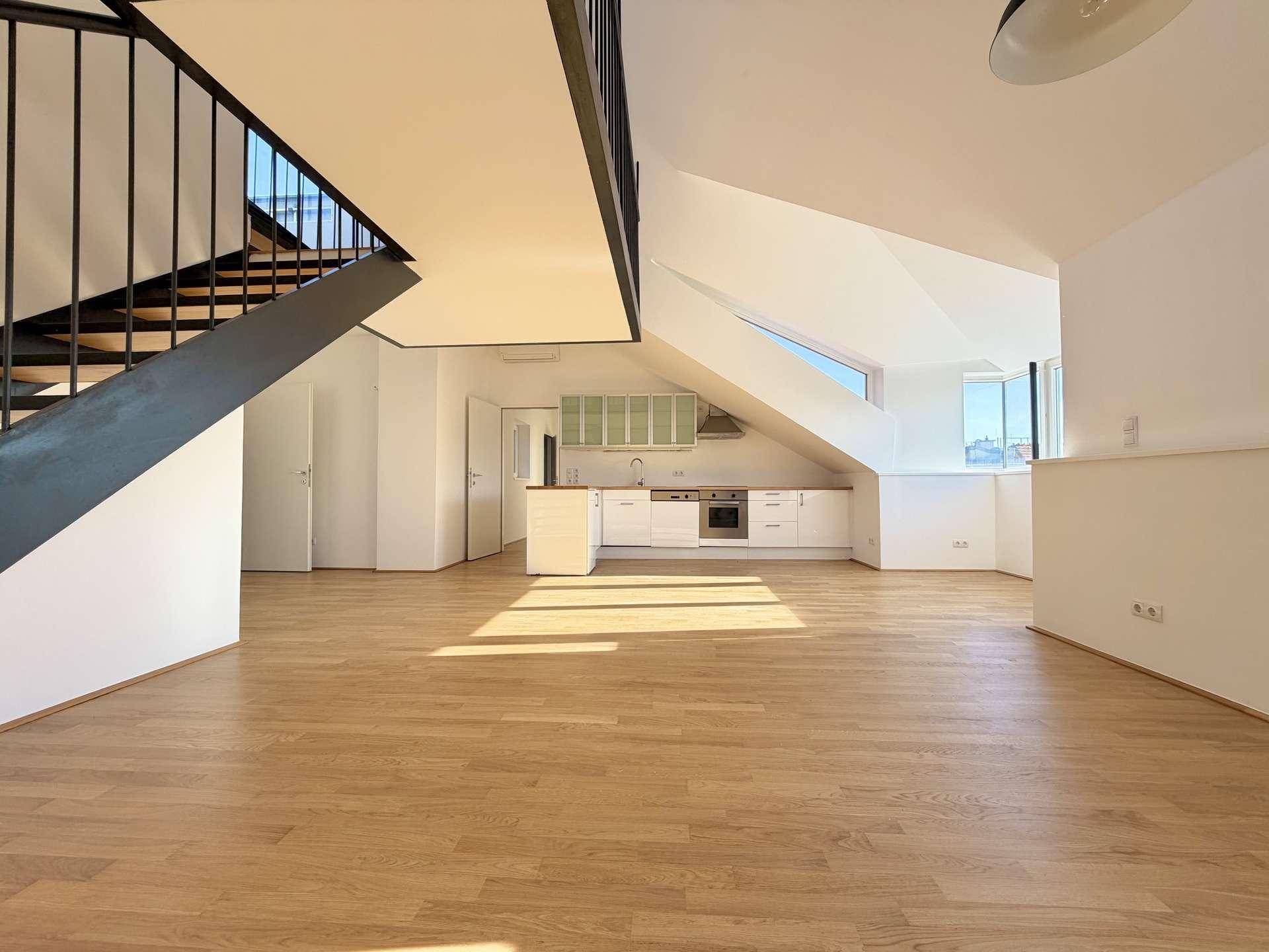 Heller offener Wohnbereich mit integrierter Küche, Holzfußboden und moderner Treppe zum Obergeschoss.