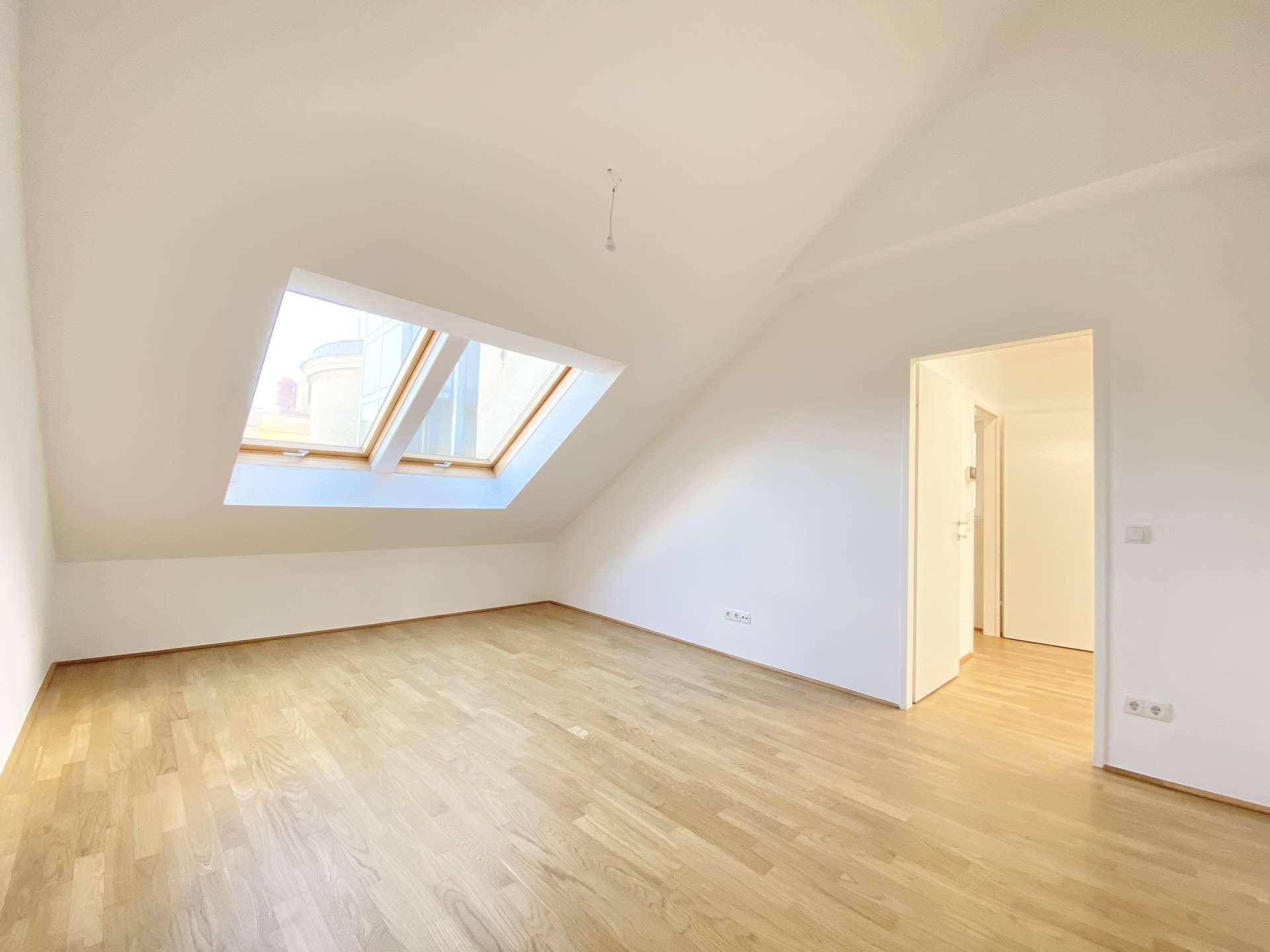 Helles Zimmer mit Holzfußboden, schrägen Wänden und Dachfenstern für viel Tageslicht.